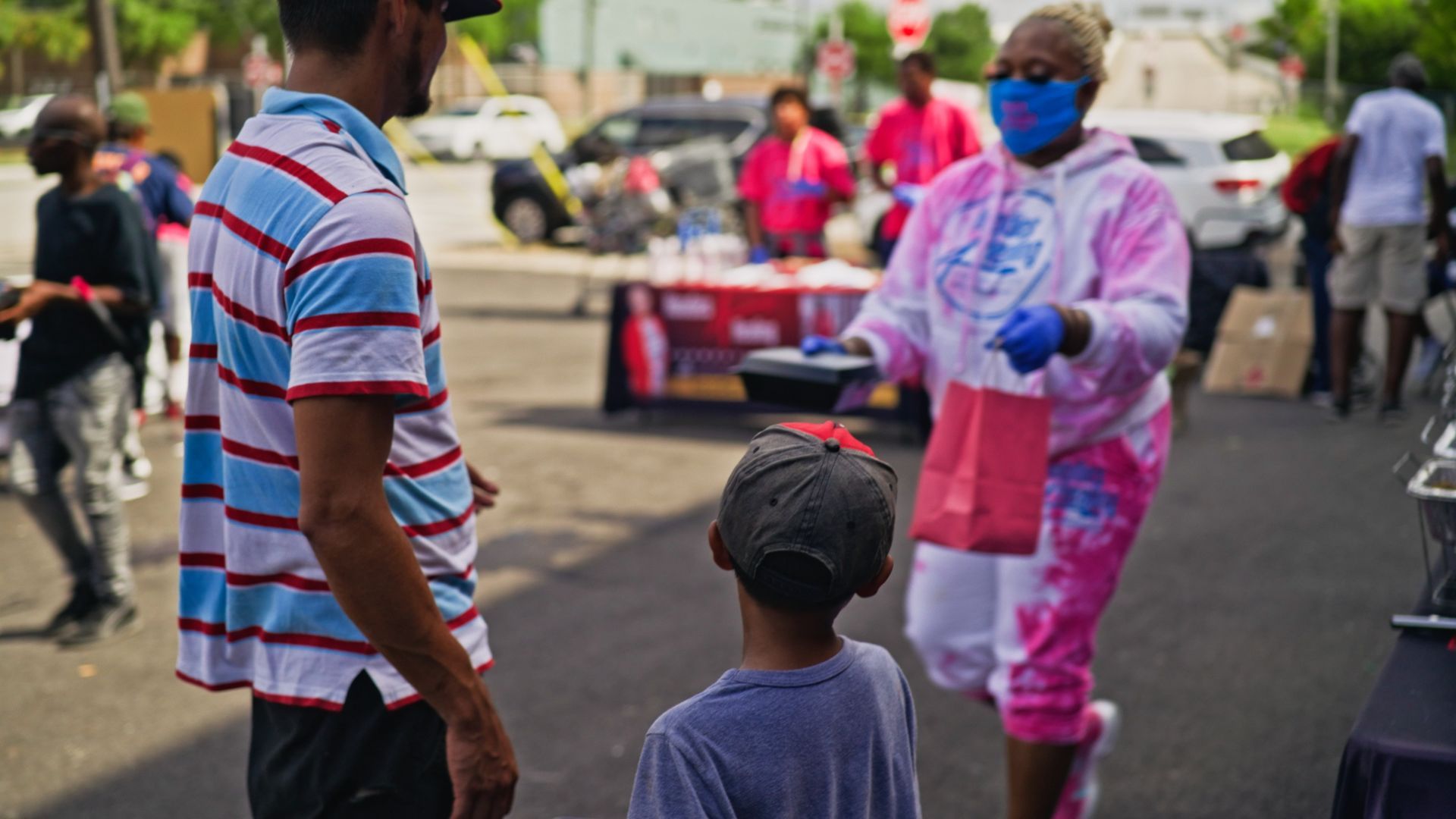 A woman wearing a mask is giving food to a child.