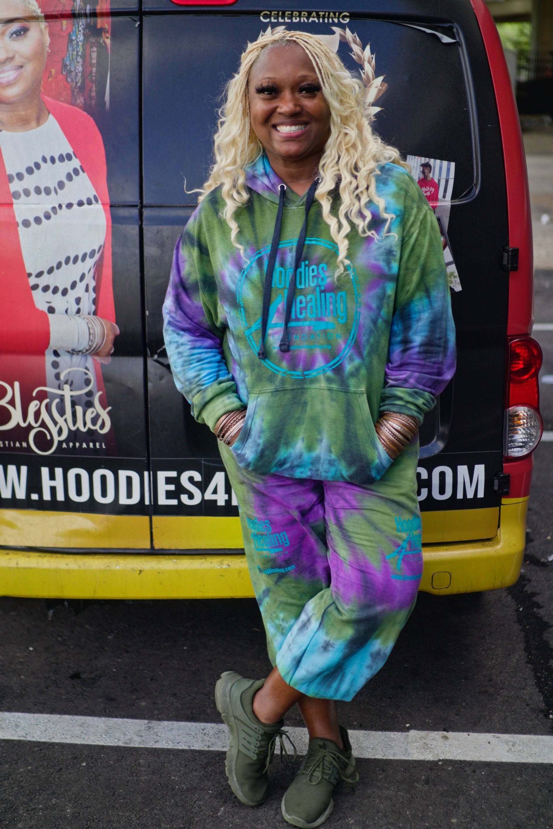 A woman in a tie dye hoodie is standing in front of a van.