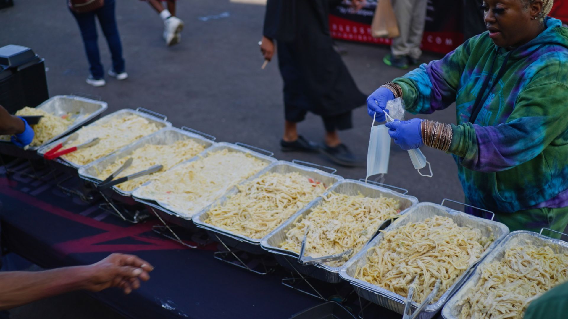 A woman is serving food at a buffet table while wearing a mask.