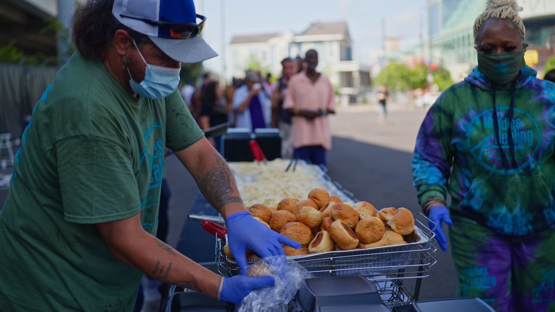 A man wearing a mask and gloves is standing next to a tray of food.