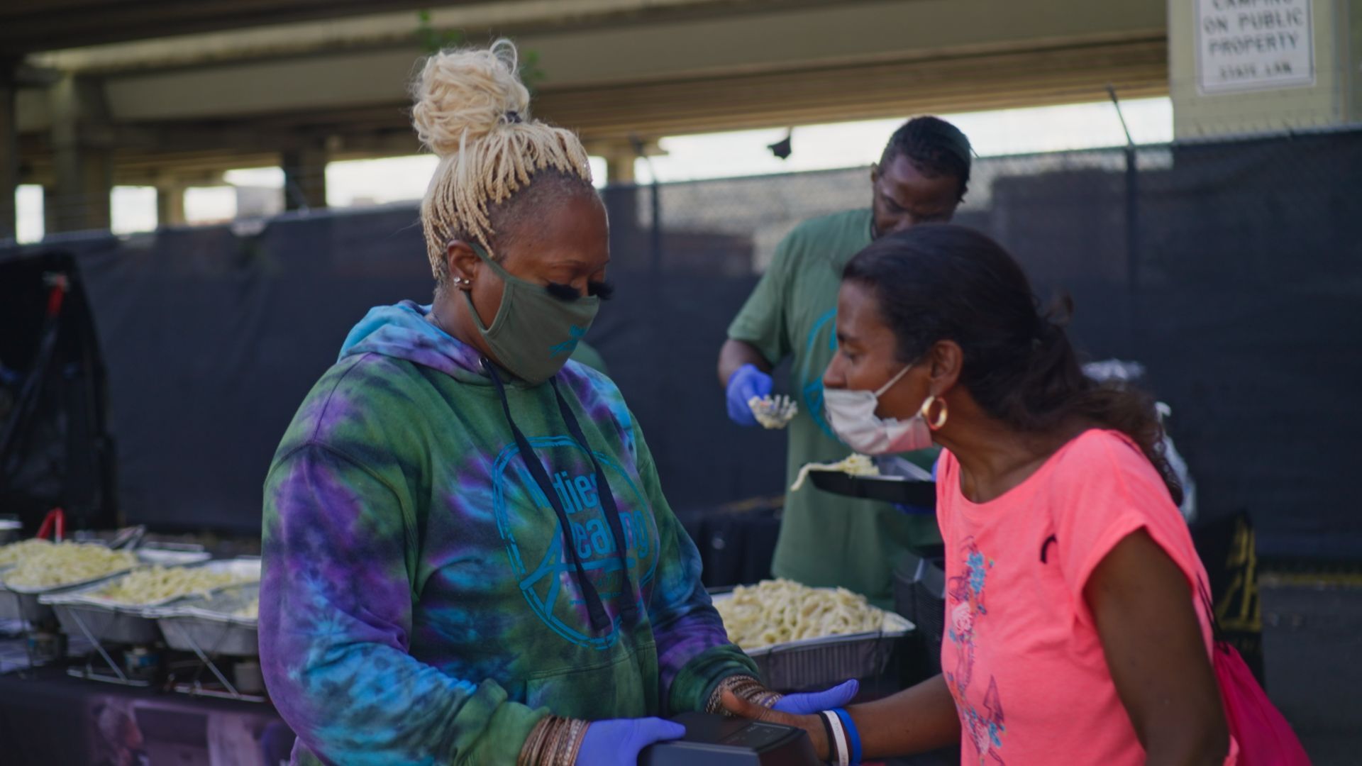 A woman wearing a mask is giving food to another woman.