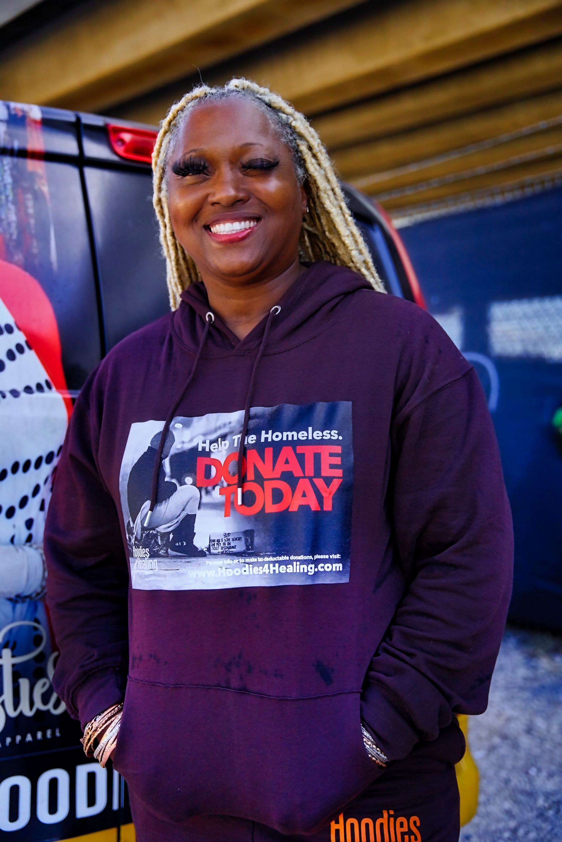 A woman wearing a purple hoodie is standing in front of a van.