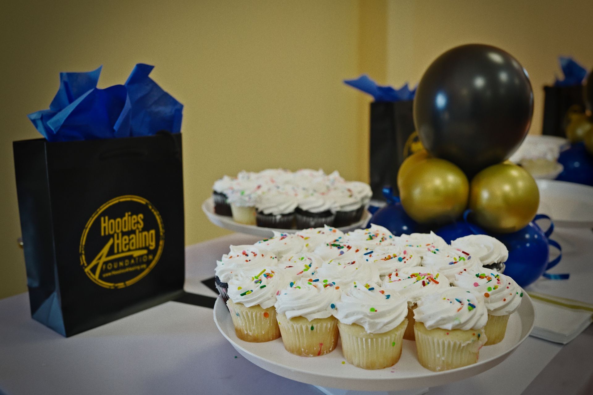 A table topped with cupcakes , balloons , and a bag of tissue paper.