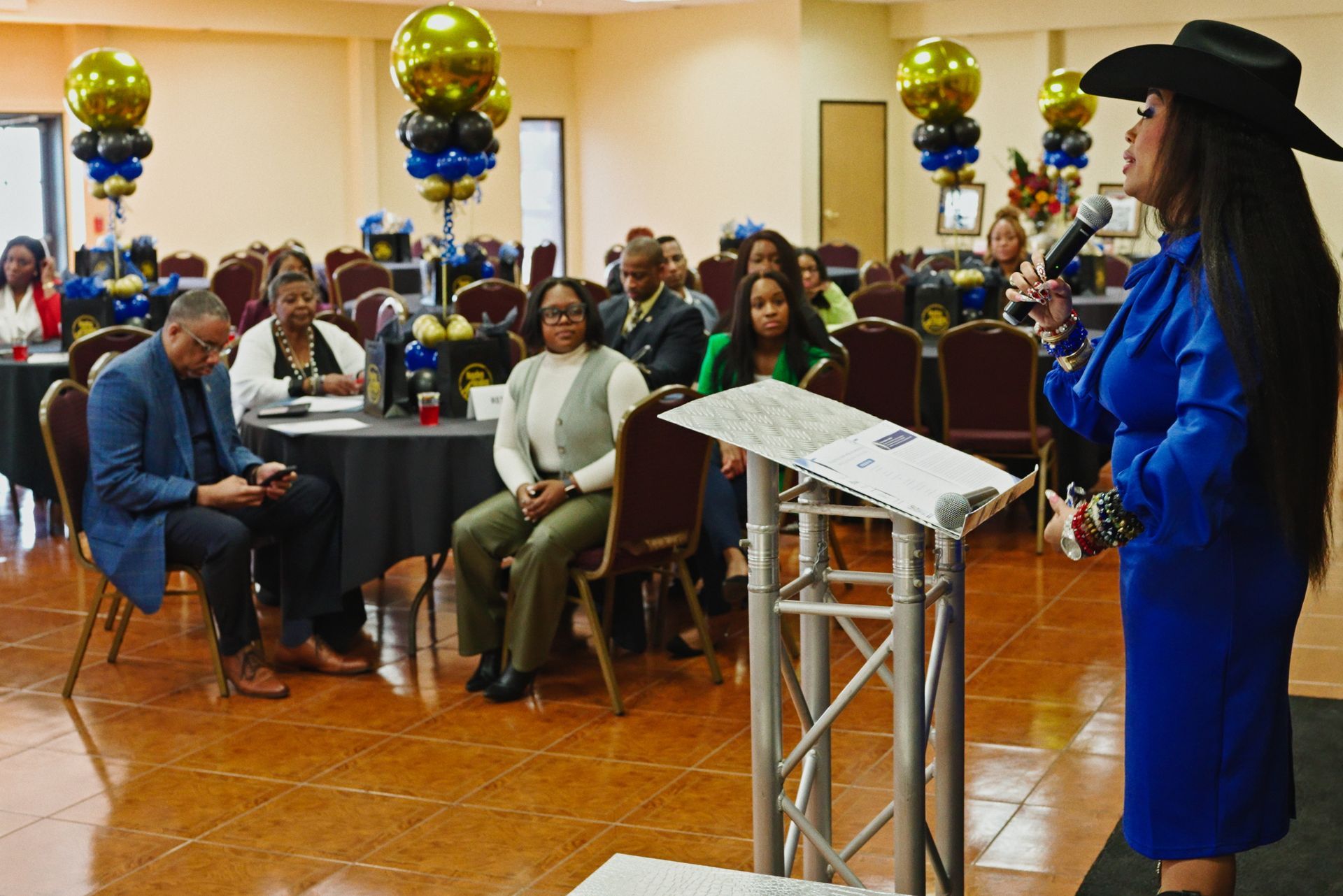 A woman in a blue dress and cowboy hat is standing at a podium giving a speech.