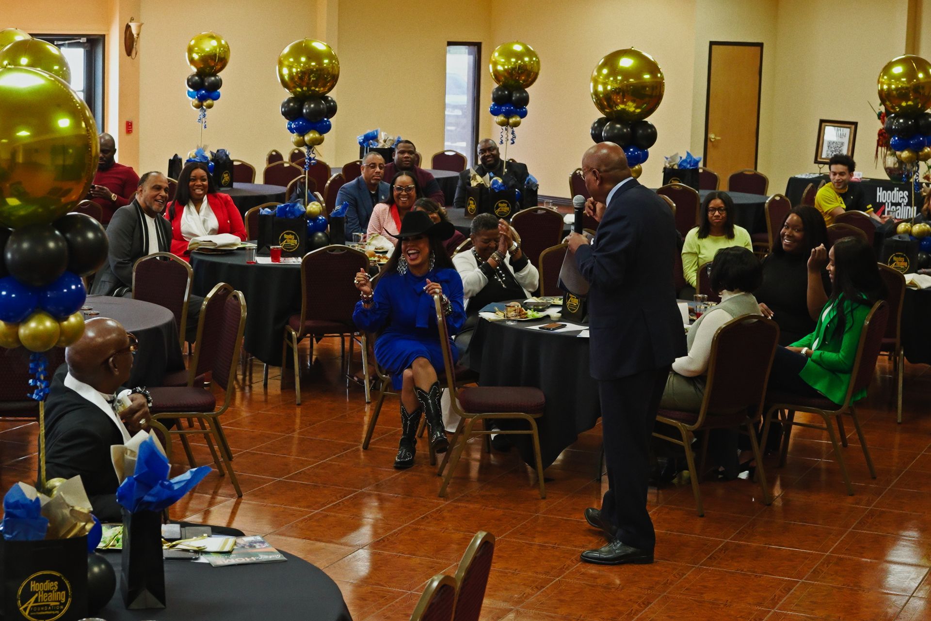 A group of people are sitting at tables in a room with balloons.