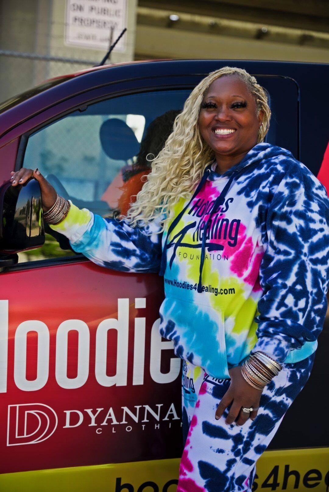 A woman in a tie dye hoodie is standing next to a van.