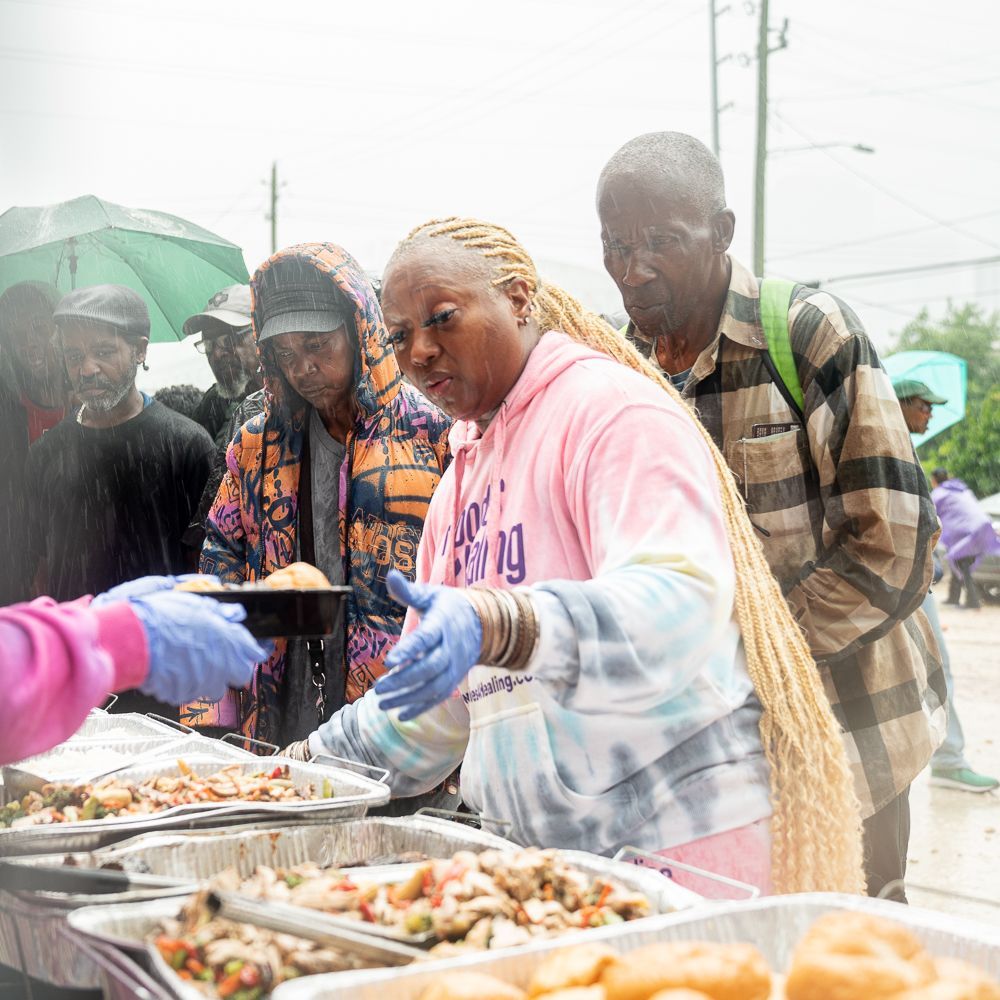 A group of people are standing around a table eating food.