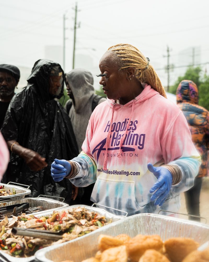 A woman in a pink hoodie is standing in front of a tray of food.