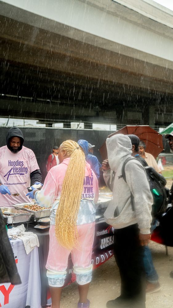 A group of people are standing around a table in the rain.