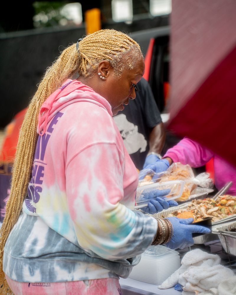 A woman in a pink tie dye hoodie is preparing food at a table.