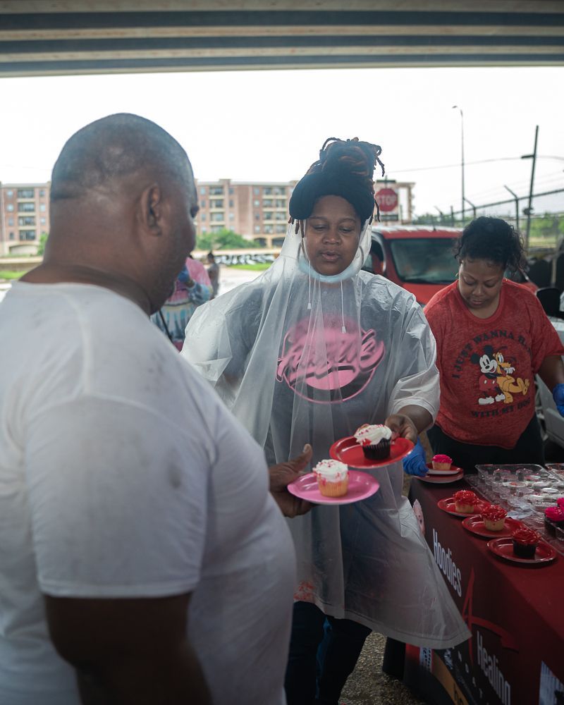 A woman in a coca cola shirt is holding a plate of cupcakes