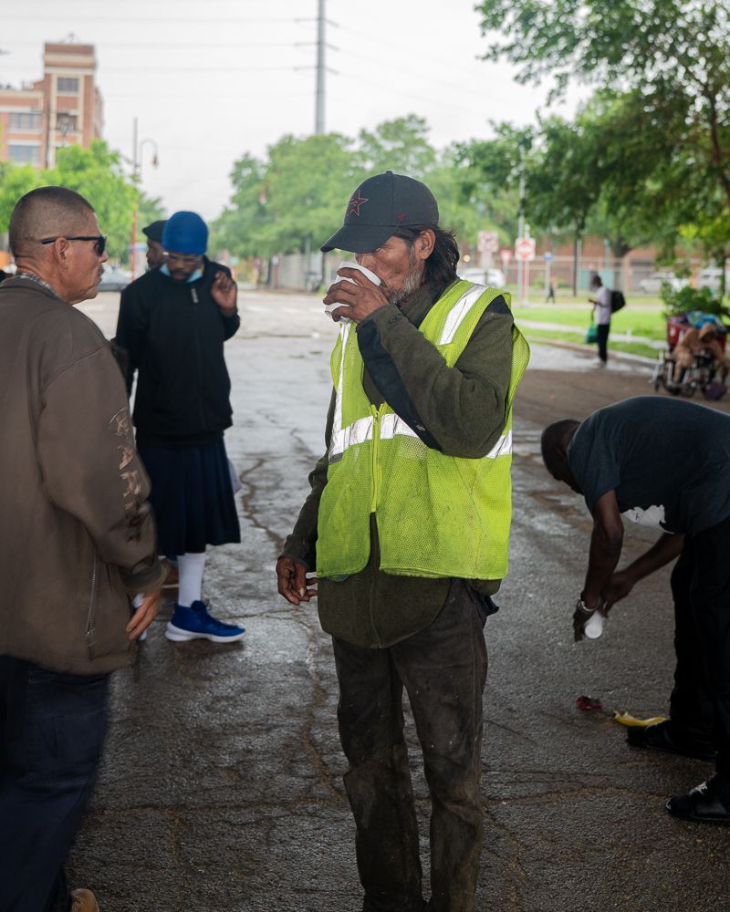 A man in a yellow vest is drinking from a cup