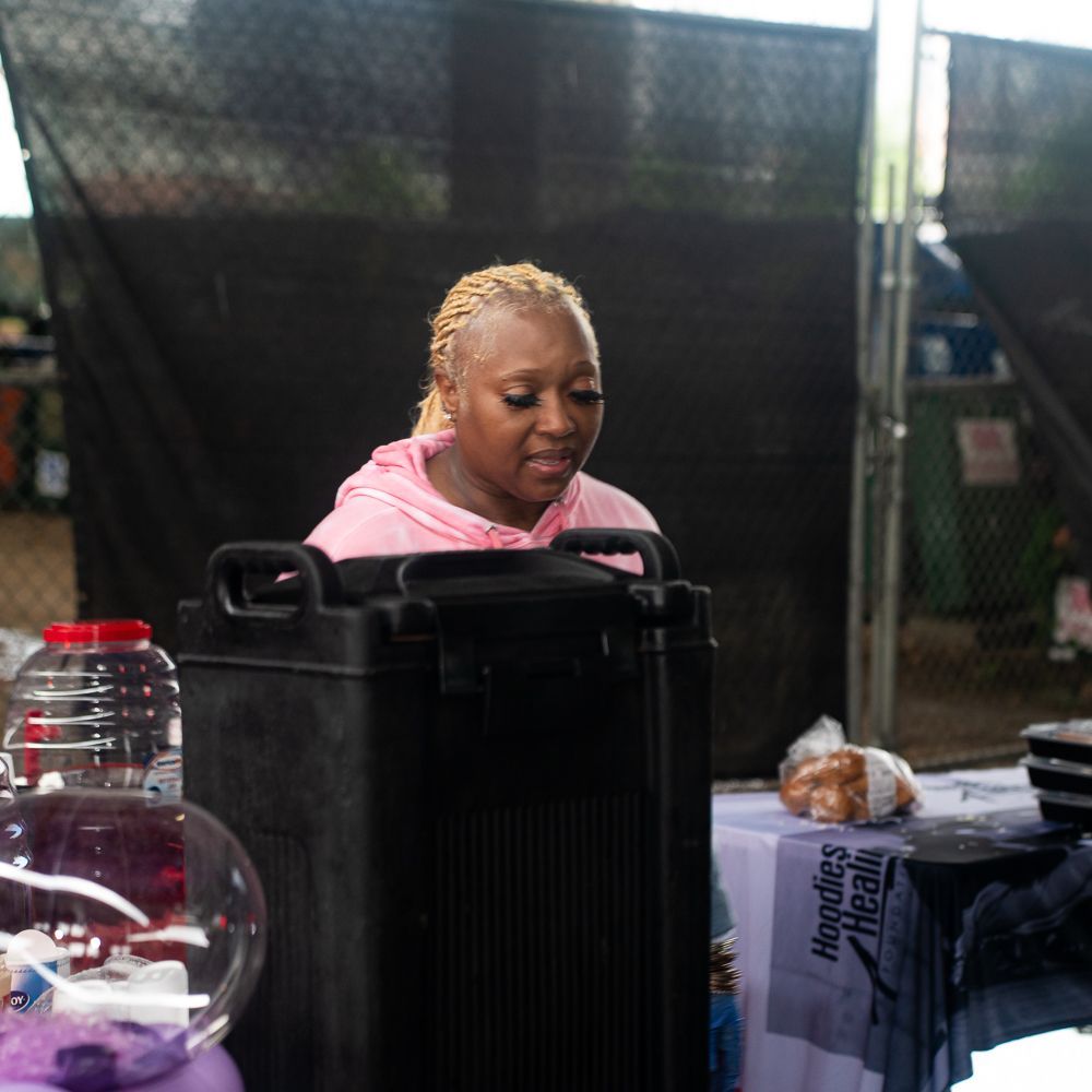 A woman in a pink hoodie sits at a table with a sign that says noodles dream