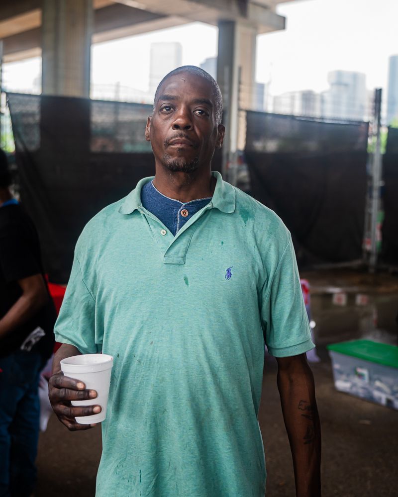 A man in a green polo shirt is holding a cup.