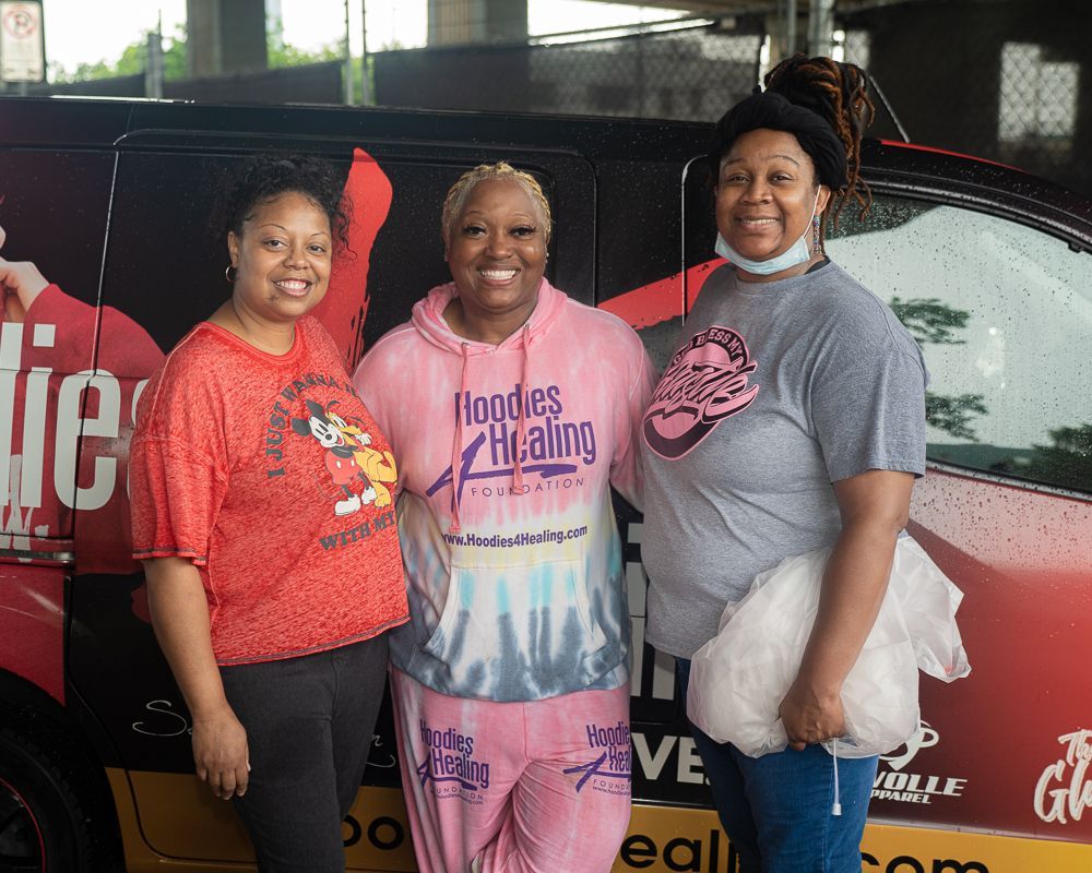 Three women are posing for a picture in front of a van that says noodles healing