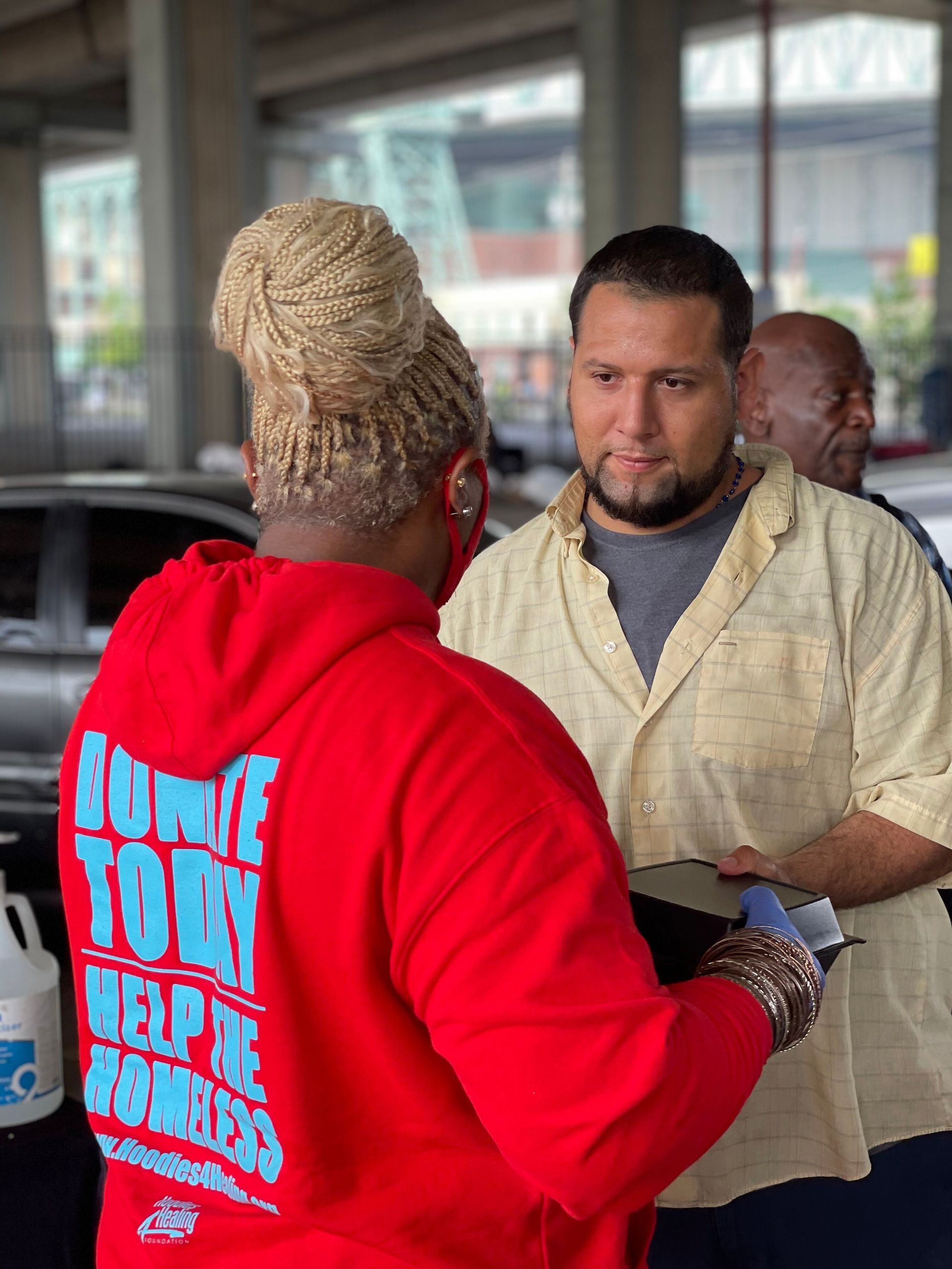 A woman in a red hoodie is talking to a man in a yellow shirt.