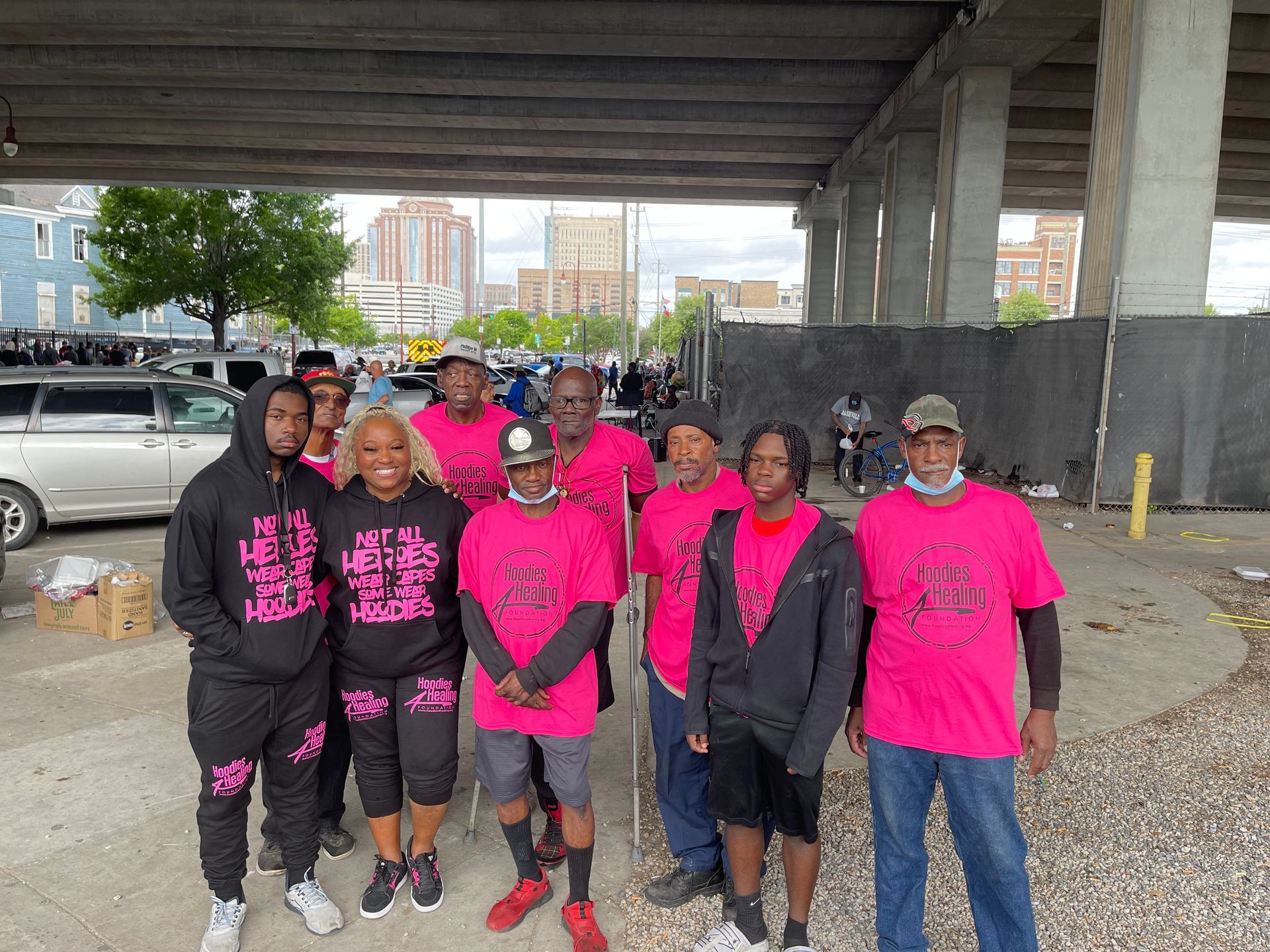 A group of men wearing pink shirts are posing for a picture under a bridge.