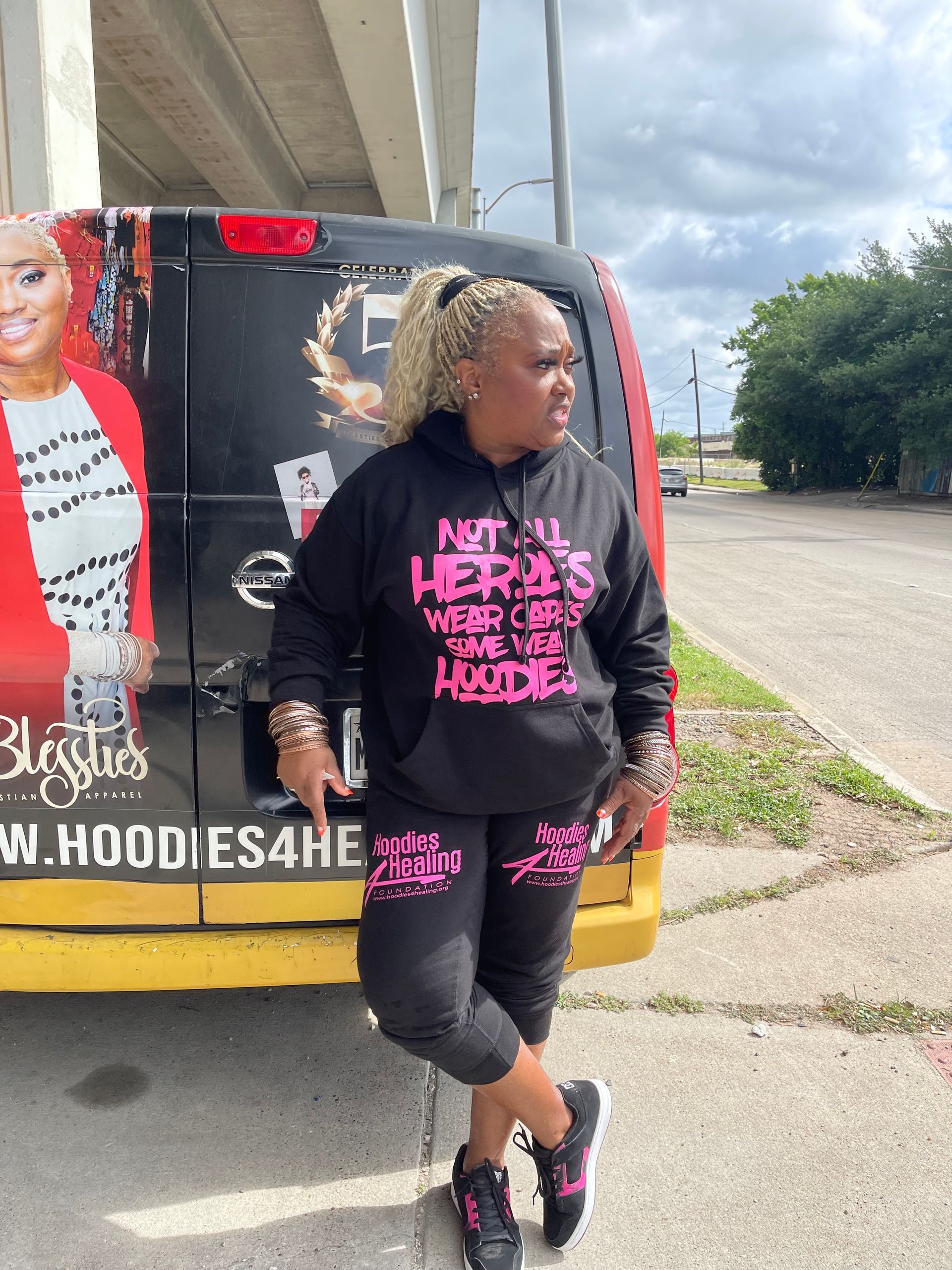 A woman in a black hoodie is standing in front of a van.