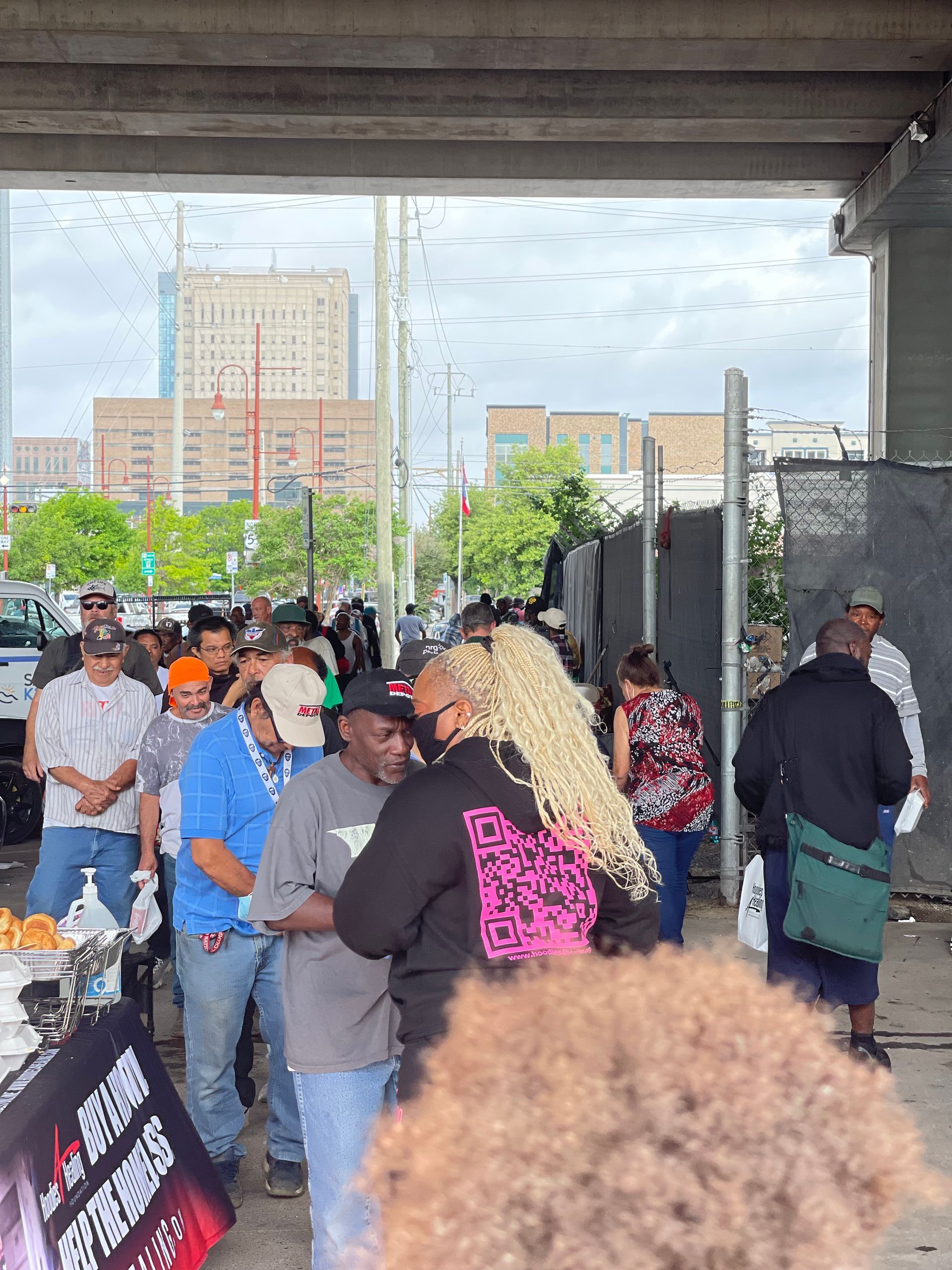 A group of people are standing in a line under a bridge.