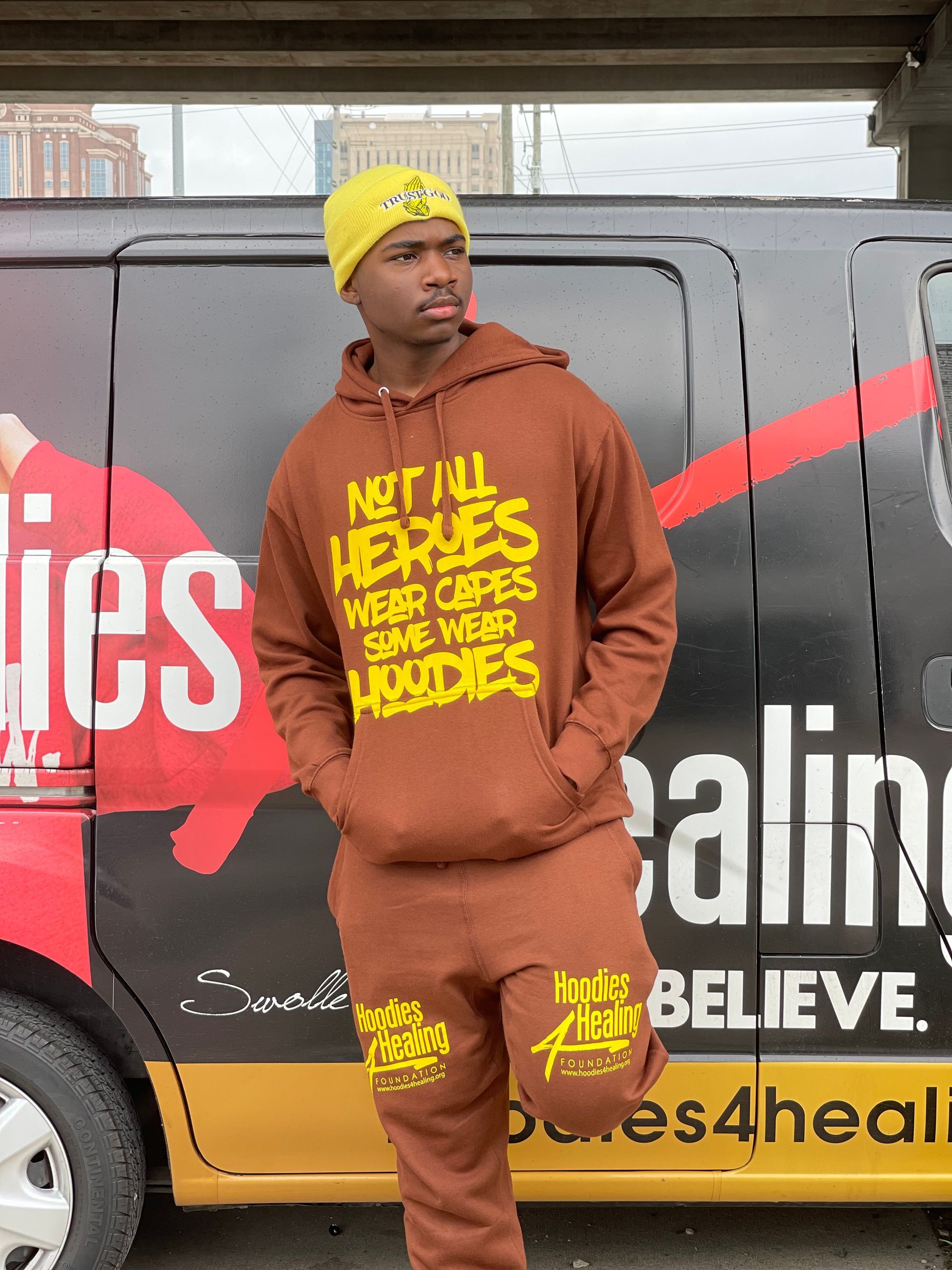 A man in a brown hoodie is standing in front of a van.
