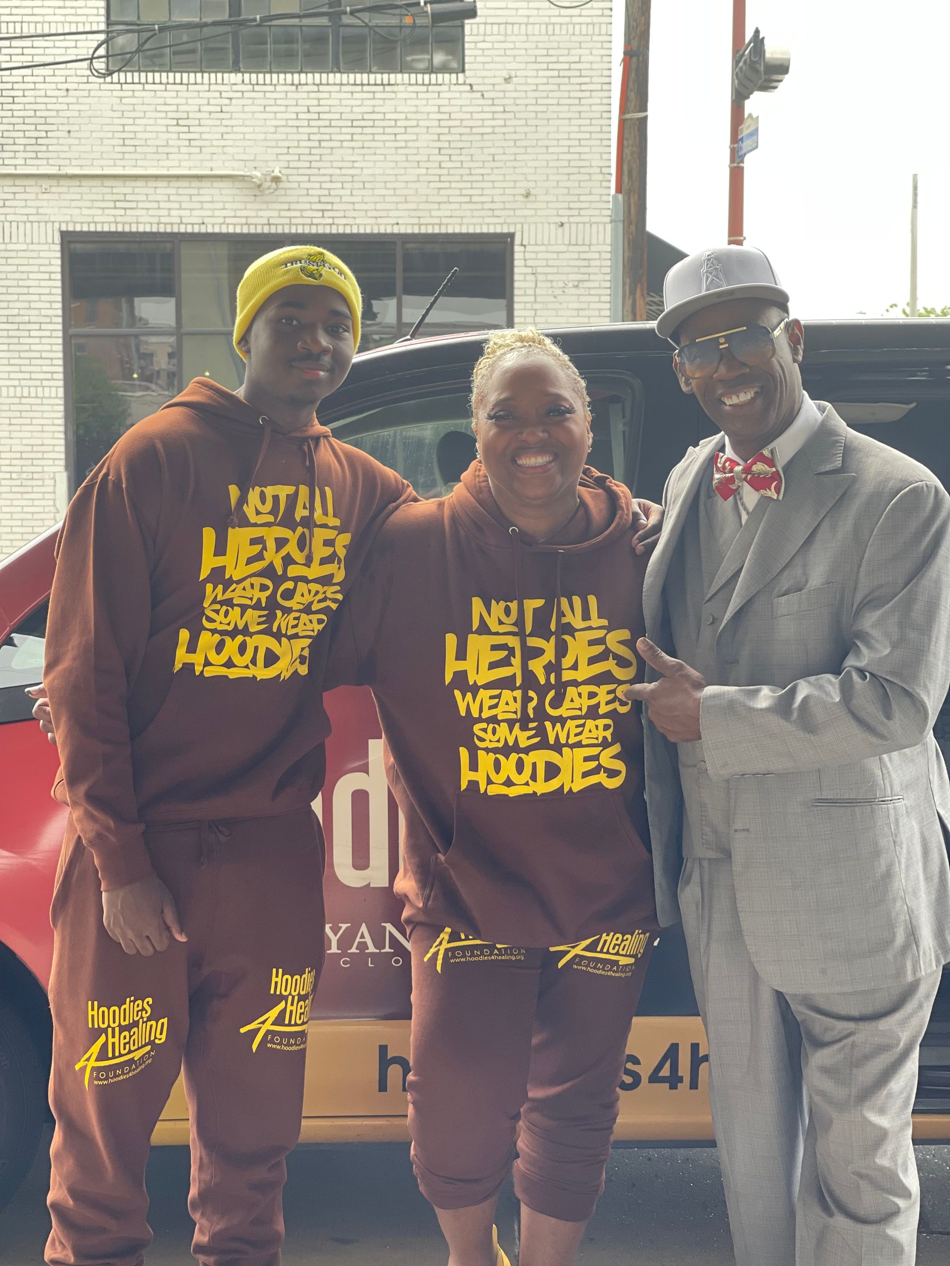Two men and a woman are posing for a picture in front of a car.