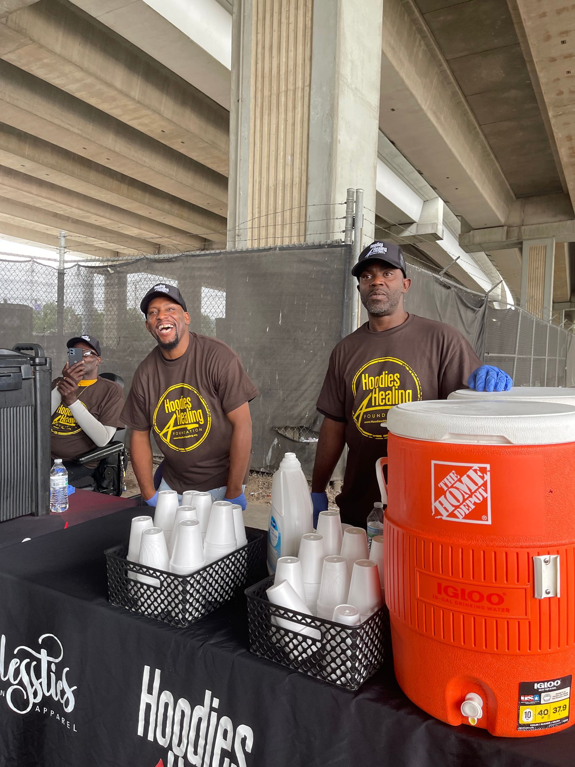 Two men are standing at a table with a large orange cooler.