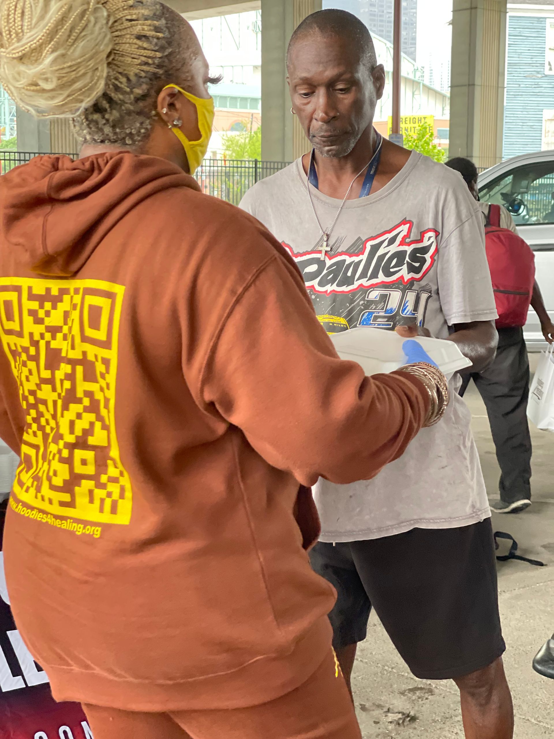 A woman wearing a mask is talking to a man wearing a phillies shirt.