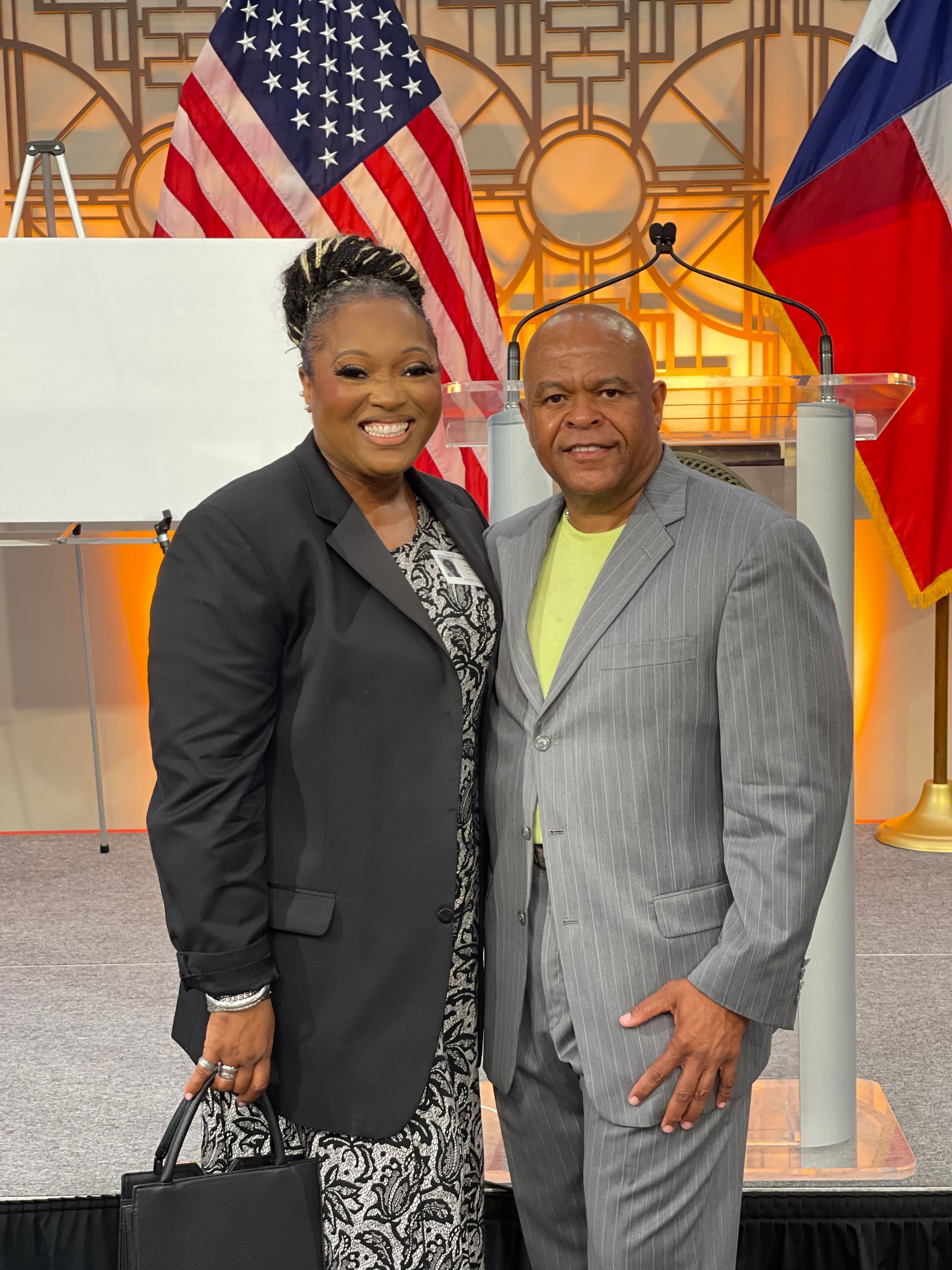 A man and a woman are posing for a picture in front of an american flag.