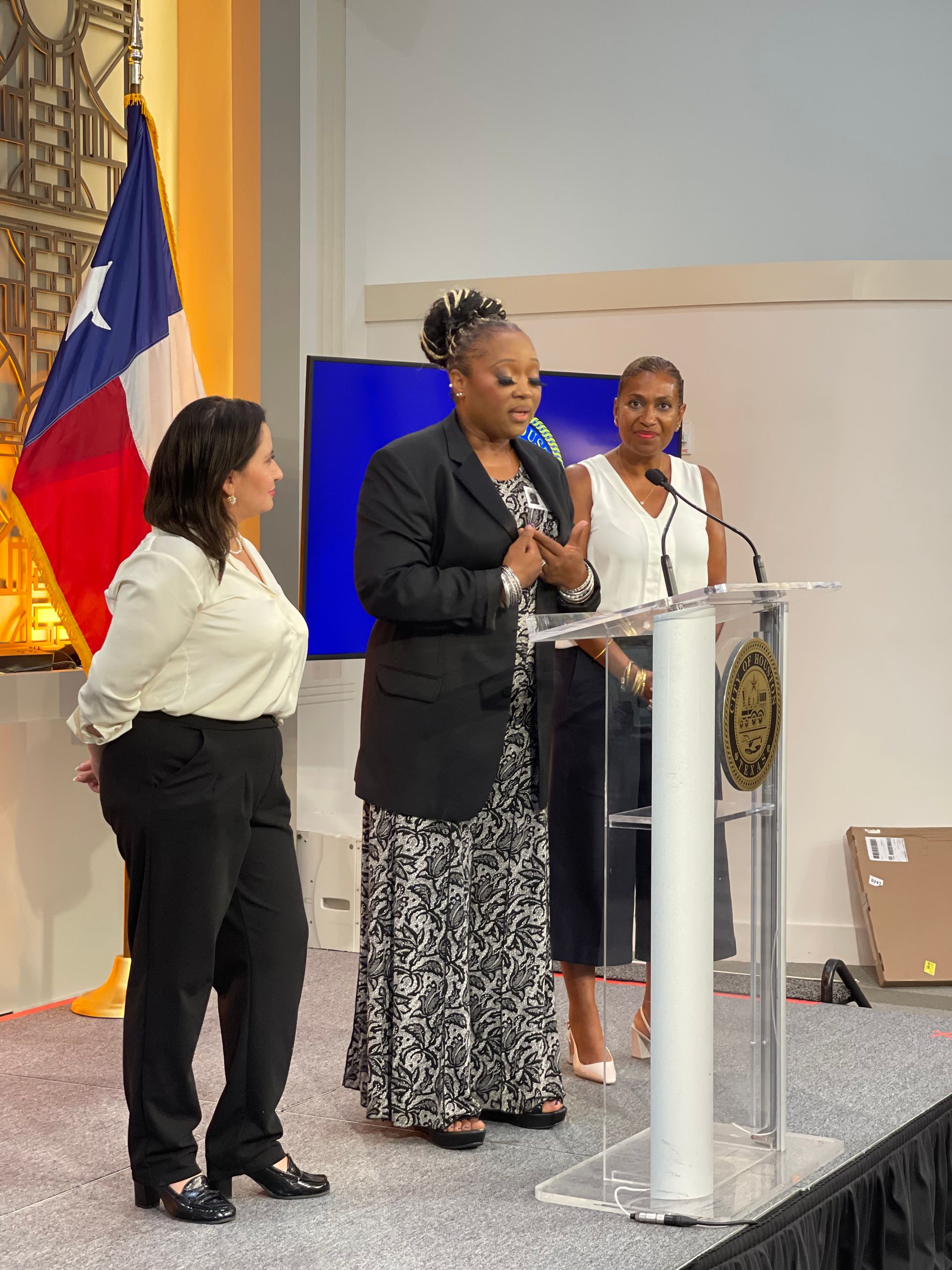 Three women are standing at a podium giving a speech.