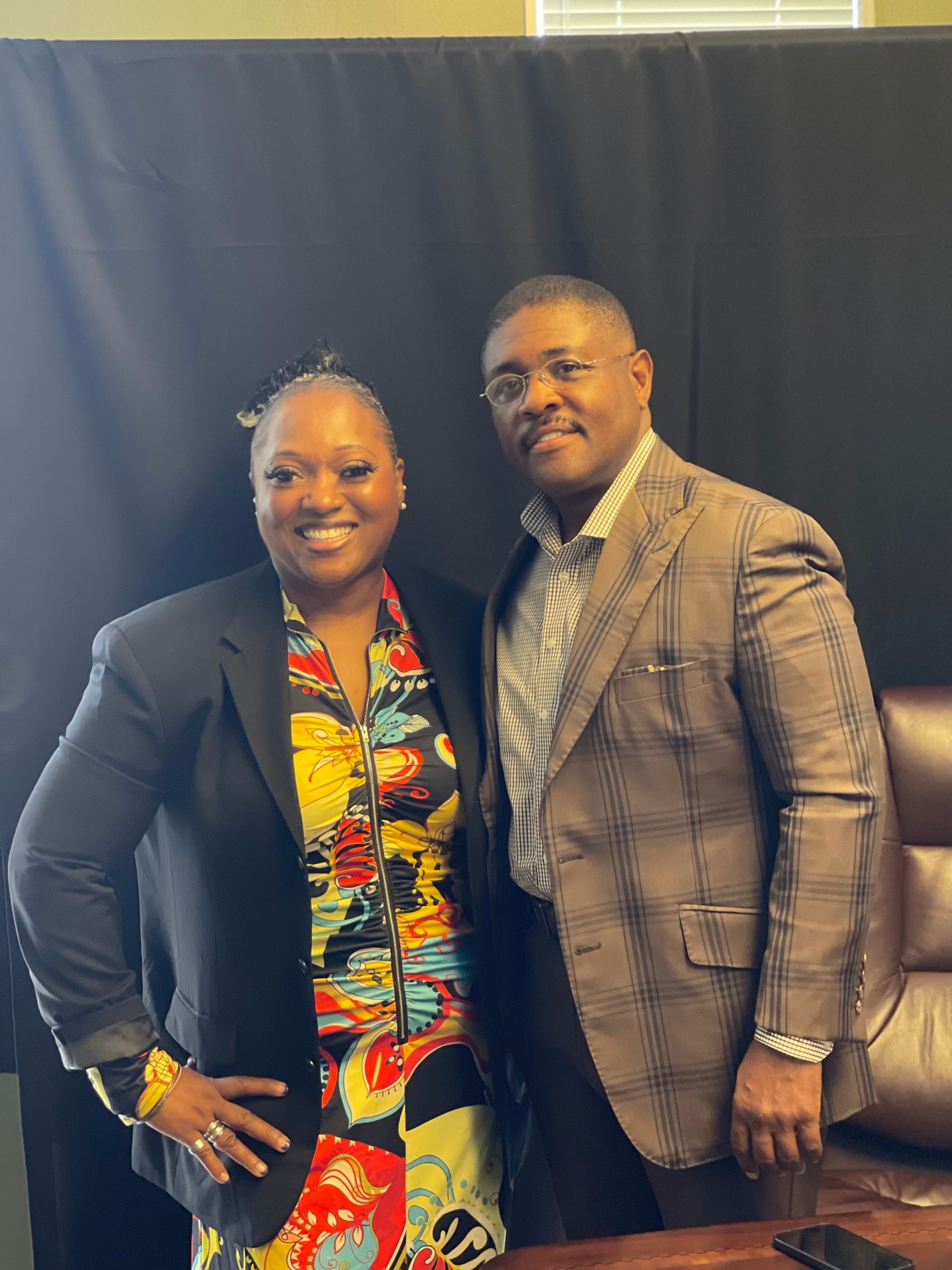 A man and a woman are posing for a picture in front of a black curtain.