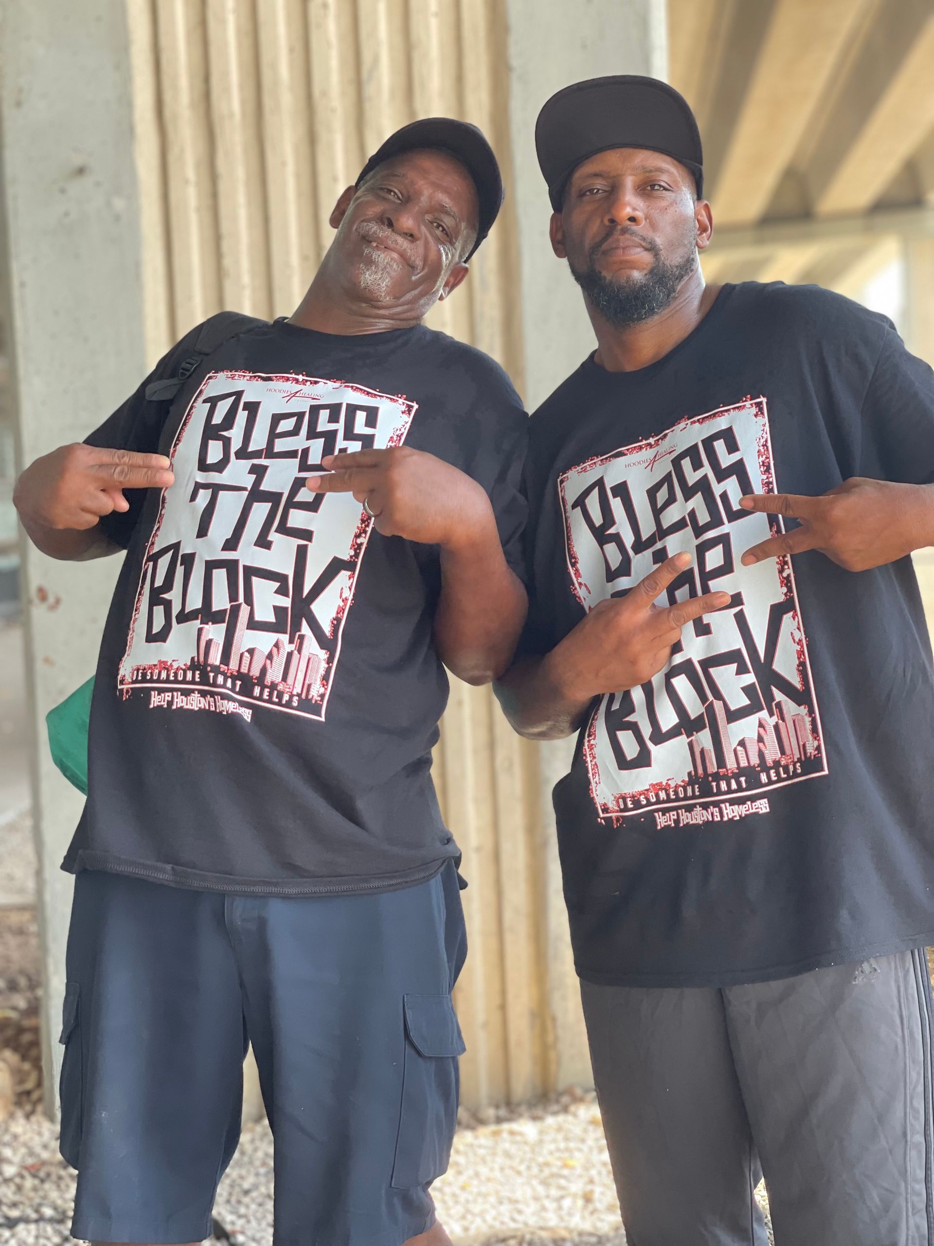 Two men wearing black shirts that say bless the block