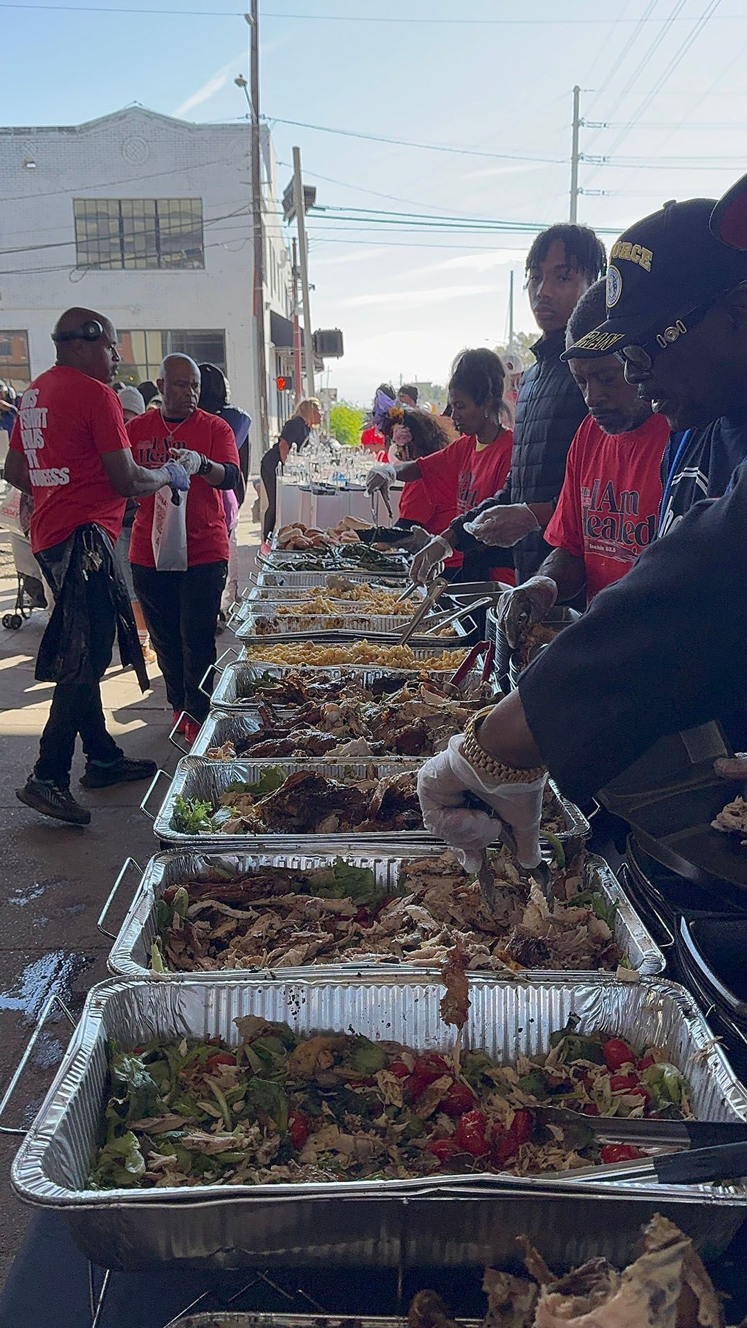 A group of people are standing around a long table filled with trays of food.