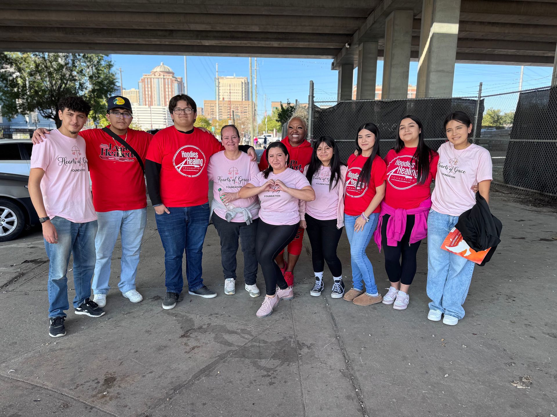 A group of people wearing pink shirts are posing for a picture under a bridge.
