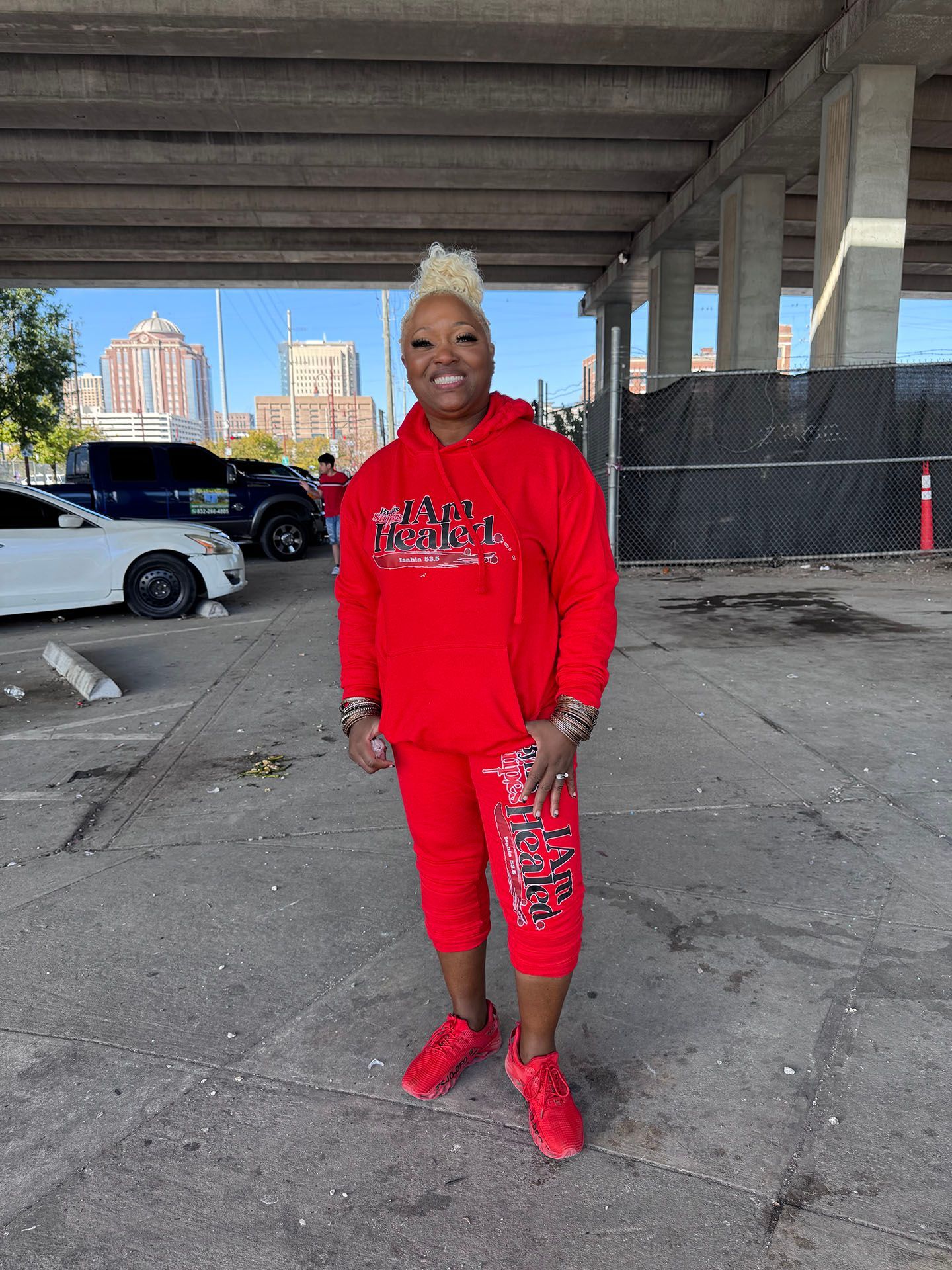 A woman in a red hoodie and red shorts is standing in a parking lot.