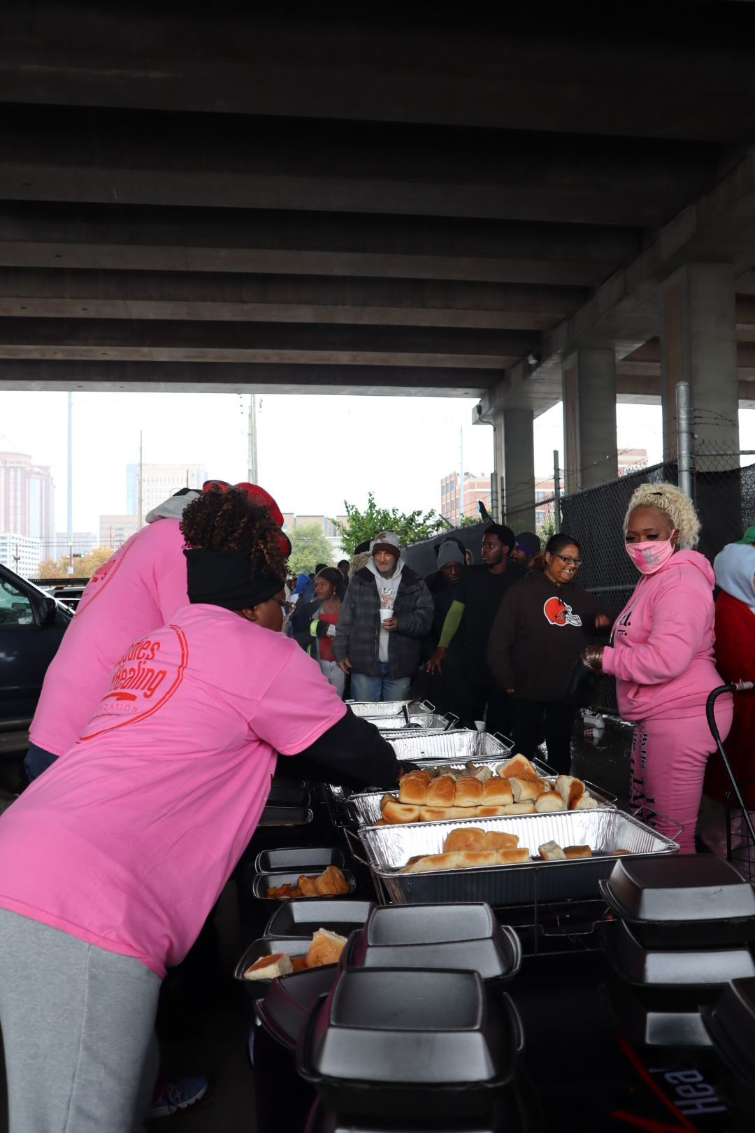 A group of people are standing around a table with trays of food.