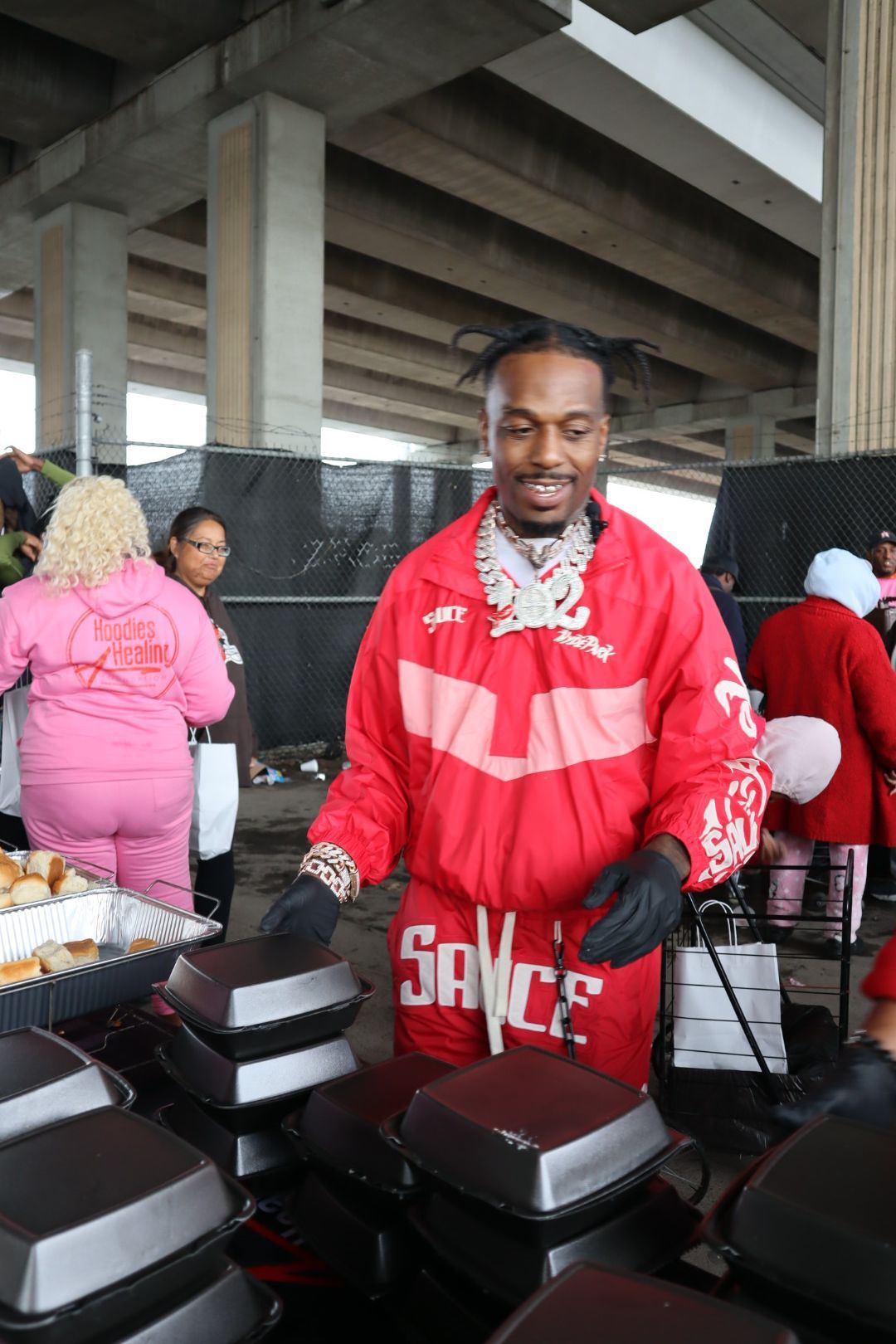A man in a red jacket is standing in front of a pile of food.