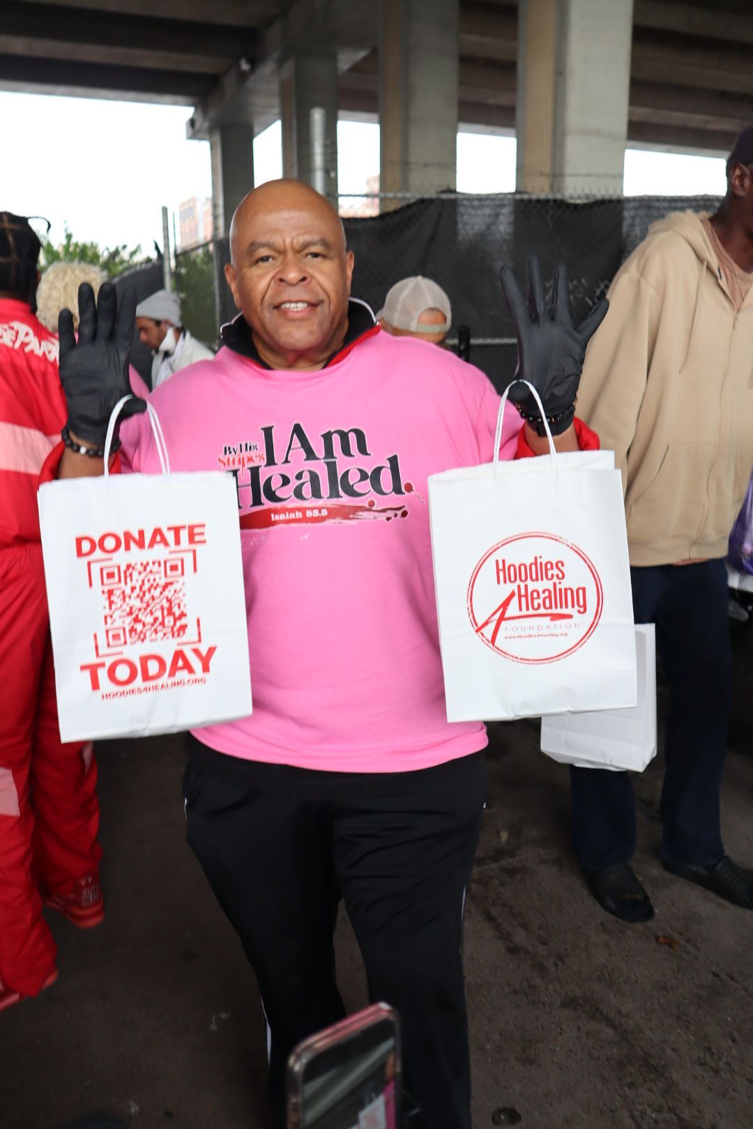 A man in a pink shirt is holding two bags that say donate today
