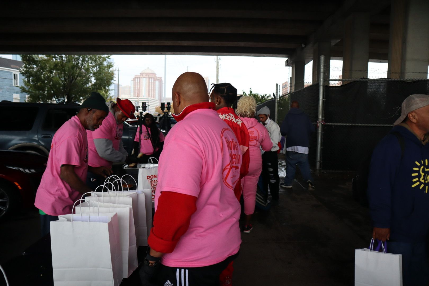 A group of people are standing under a bridge holding bags.