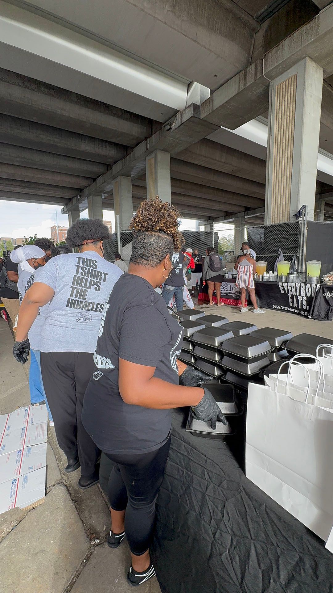 A group of people are standing around a table under a bridge.