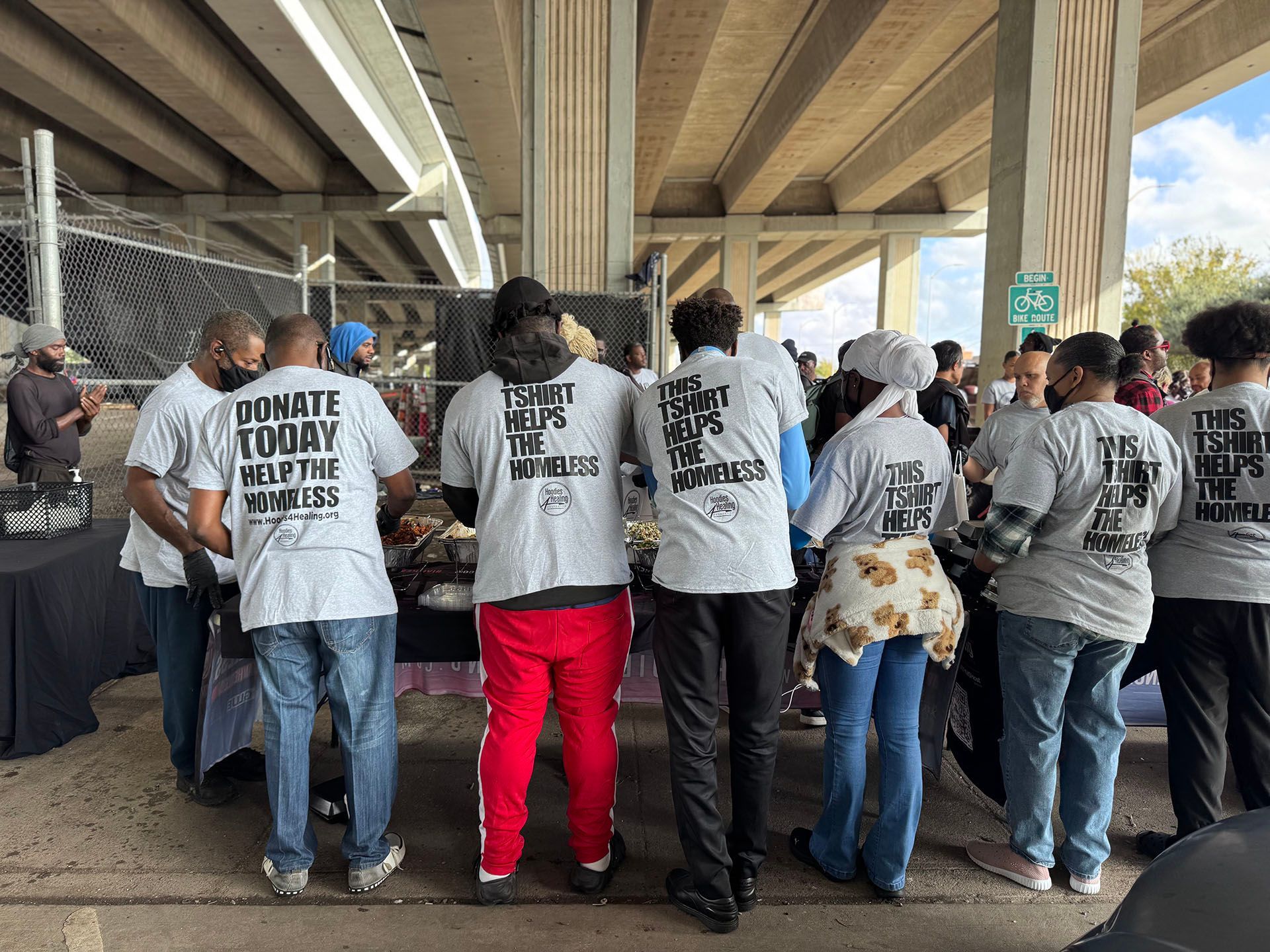 A group of people are standing around a table under a bridge.