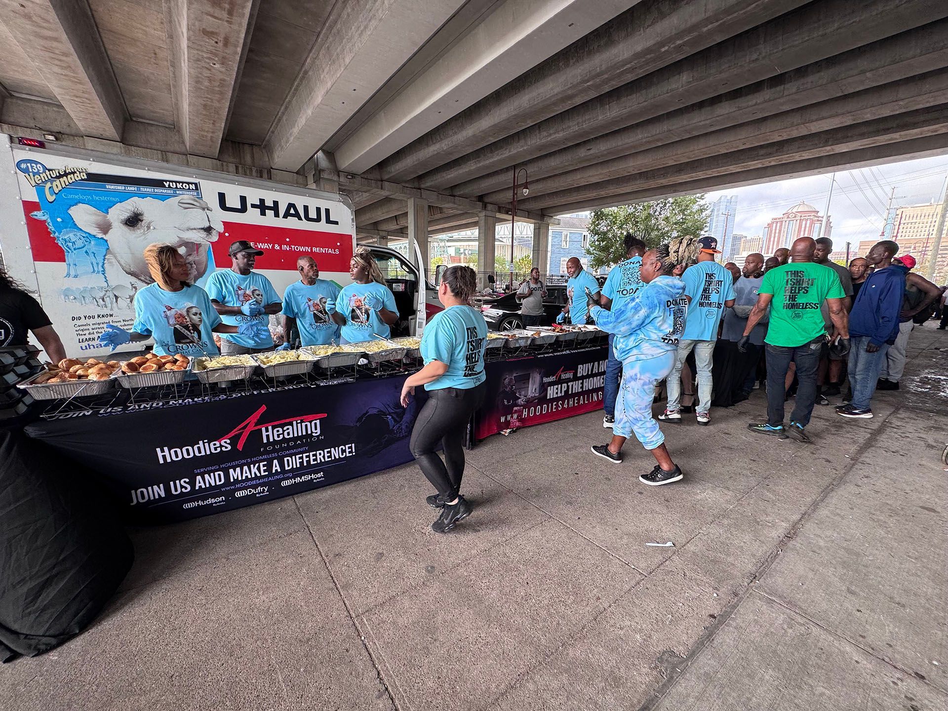 A group of people are standing around a table under a bridge.