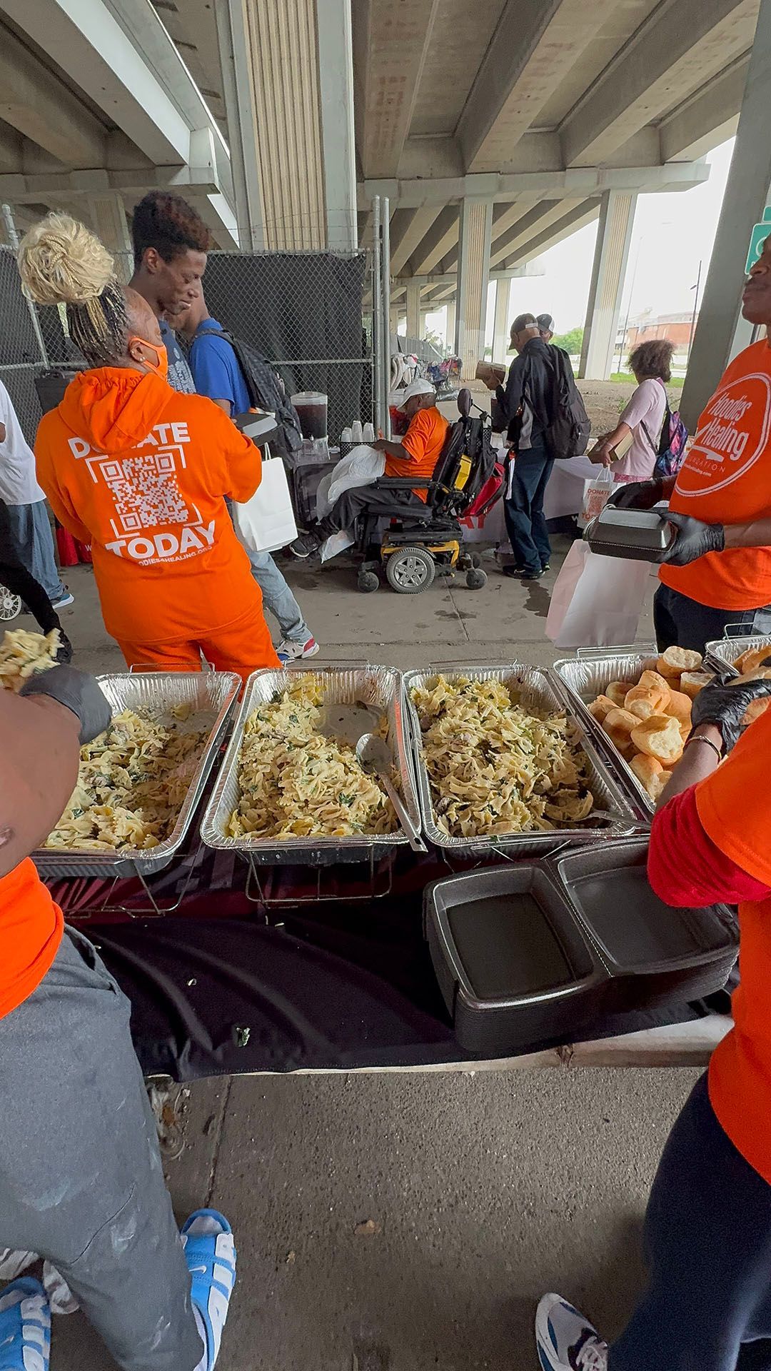 A group of people are standing around a table filled with trays of food.