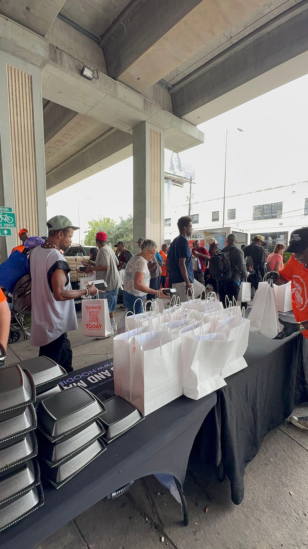 A group of people are standing around a table with bags of food.