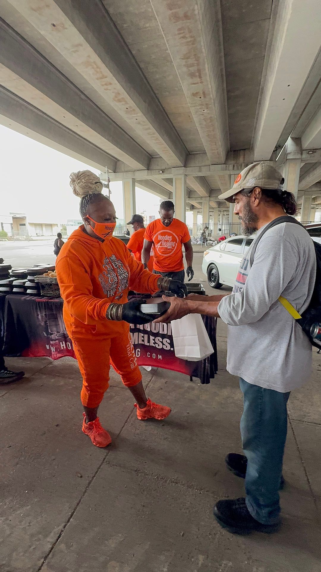 A man is giving a woman a bag of food under a bridge.