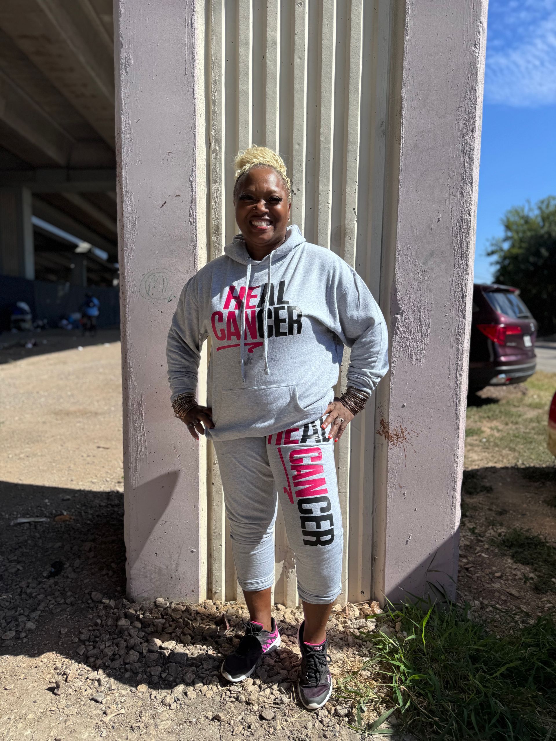 A woman wearing a hoodie and sweatpants is standing next to a pillar.