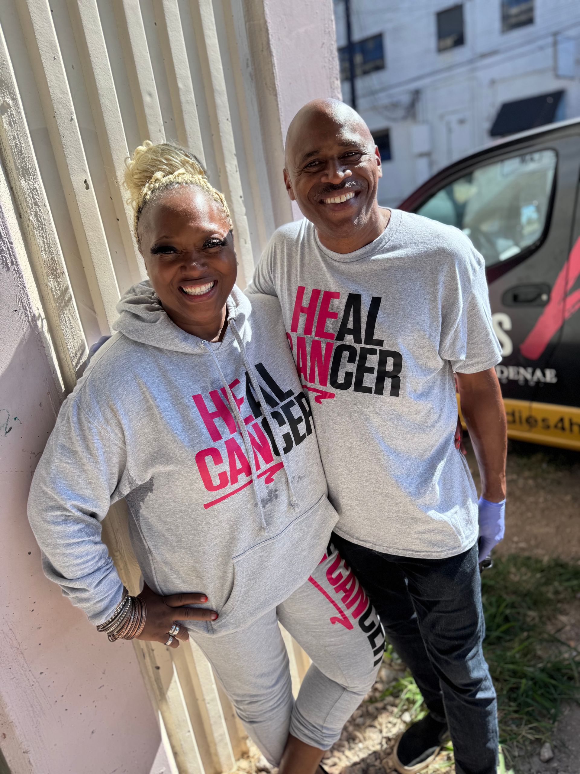 A man and a woman are standing next to each other wearing matching shirts that say `` heal cancer ''.