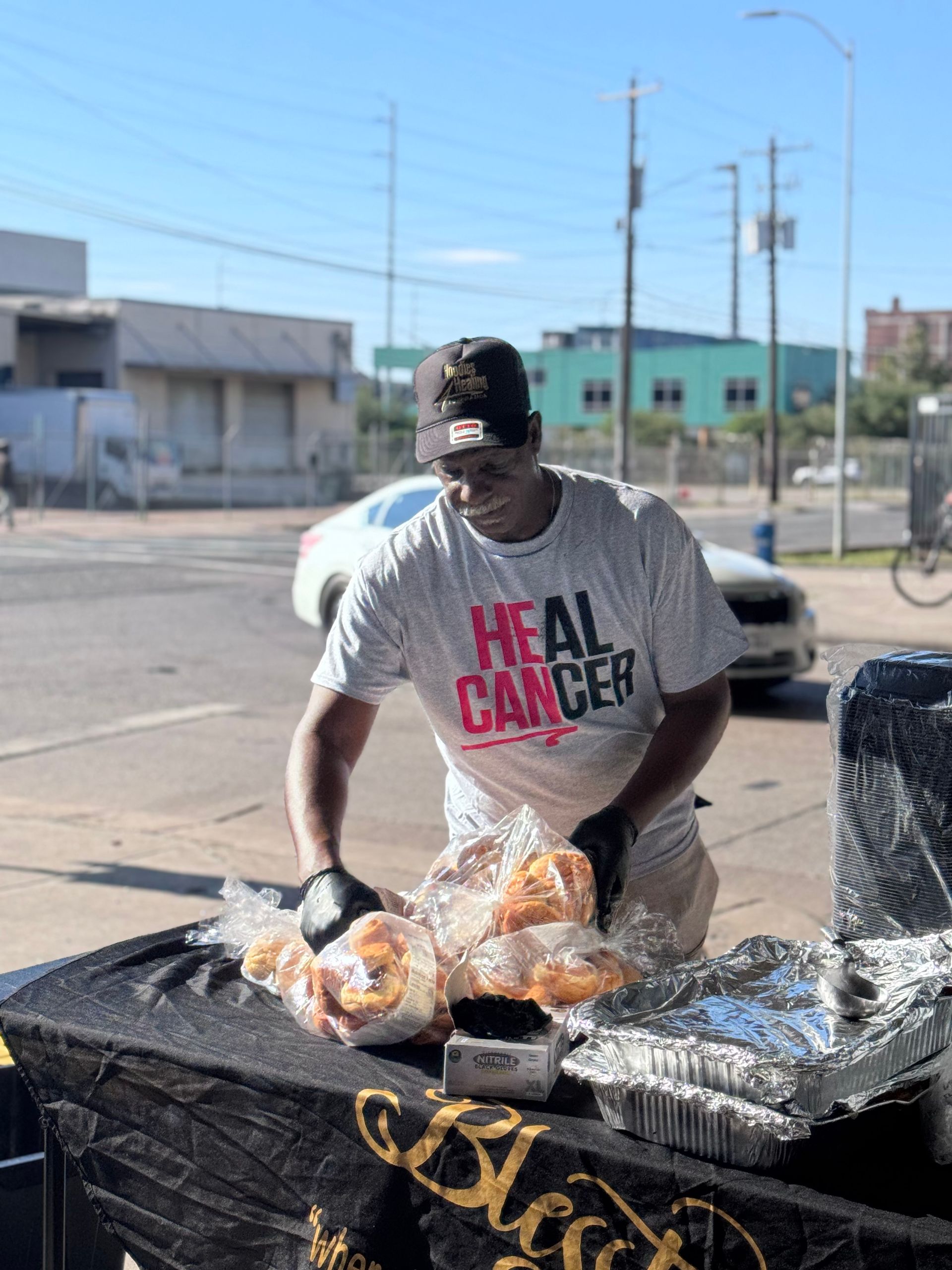 A man wearing a t-shirt that says `` heal cancer '' is preparing food on a table.