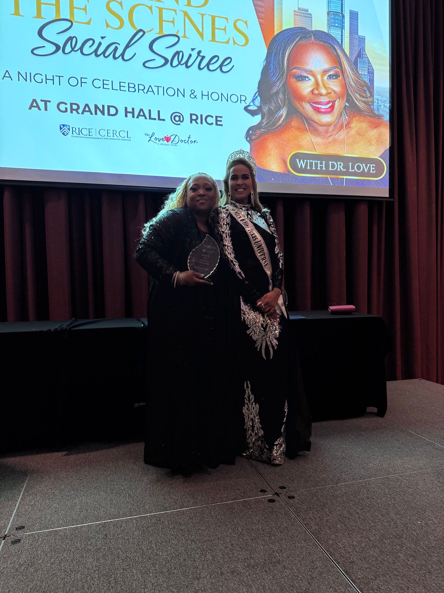 Two women are standing in front of a large screen at a social soiree.