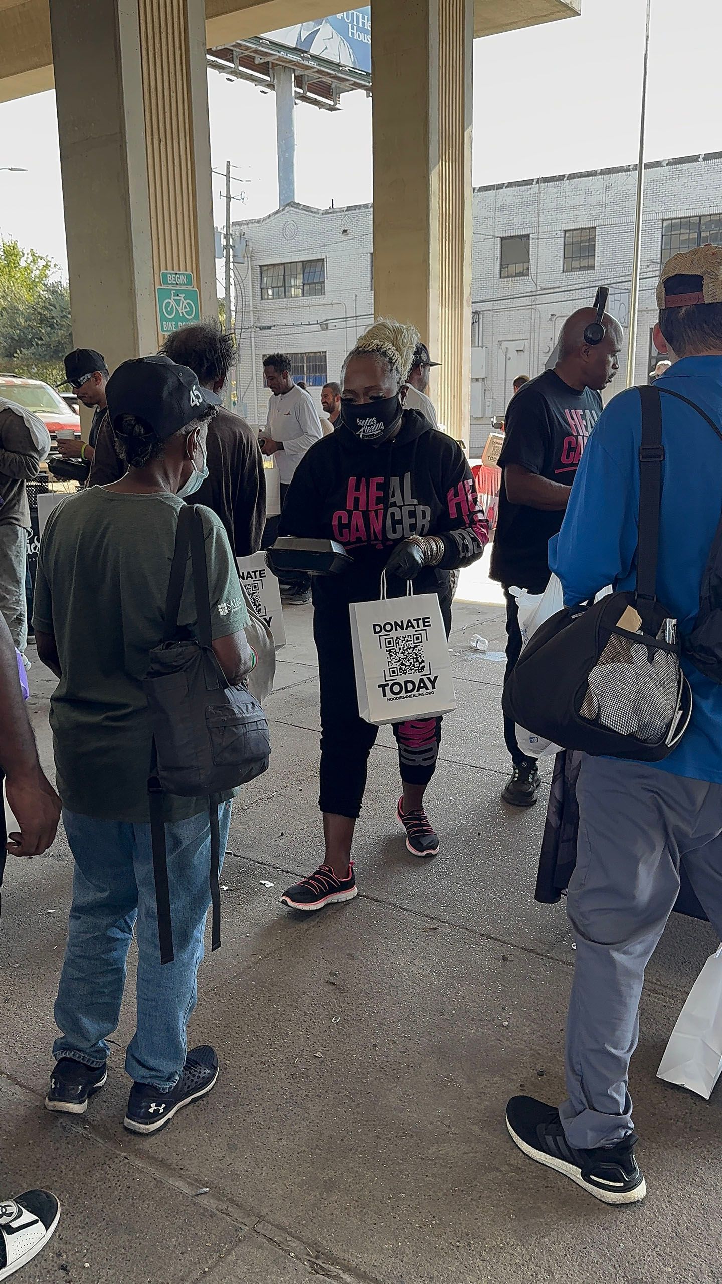A group of people are standing in a line under a bridge.