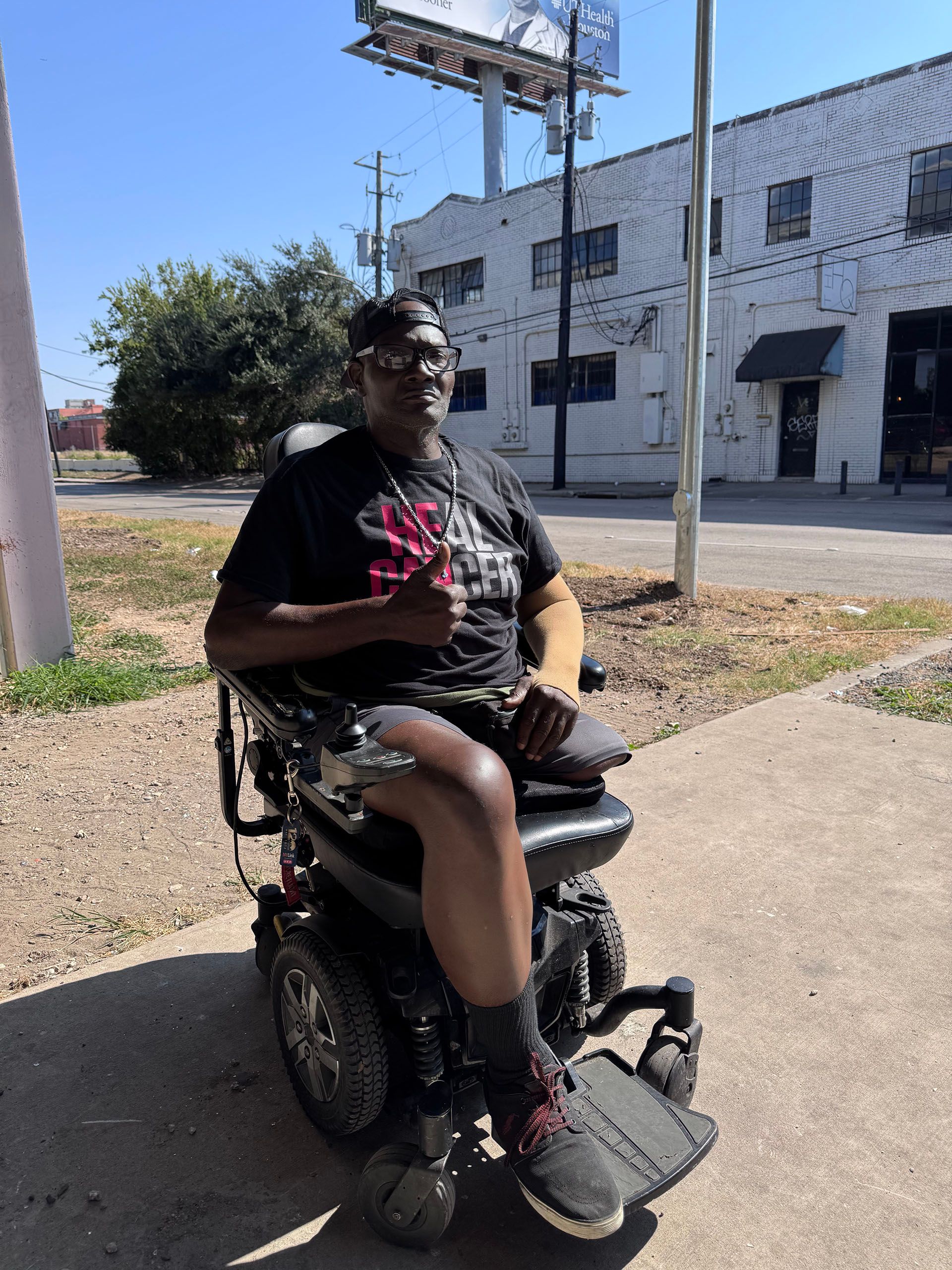 A man in a wheelchair is sitting on the sidewalk in front of a building.